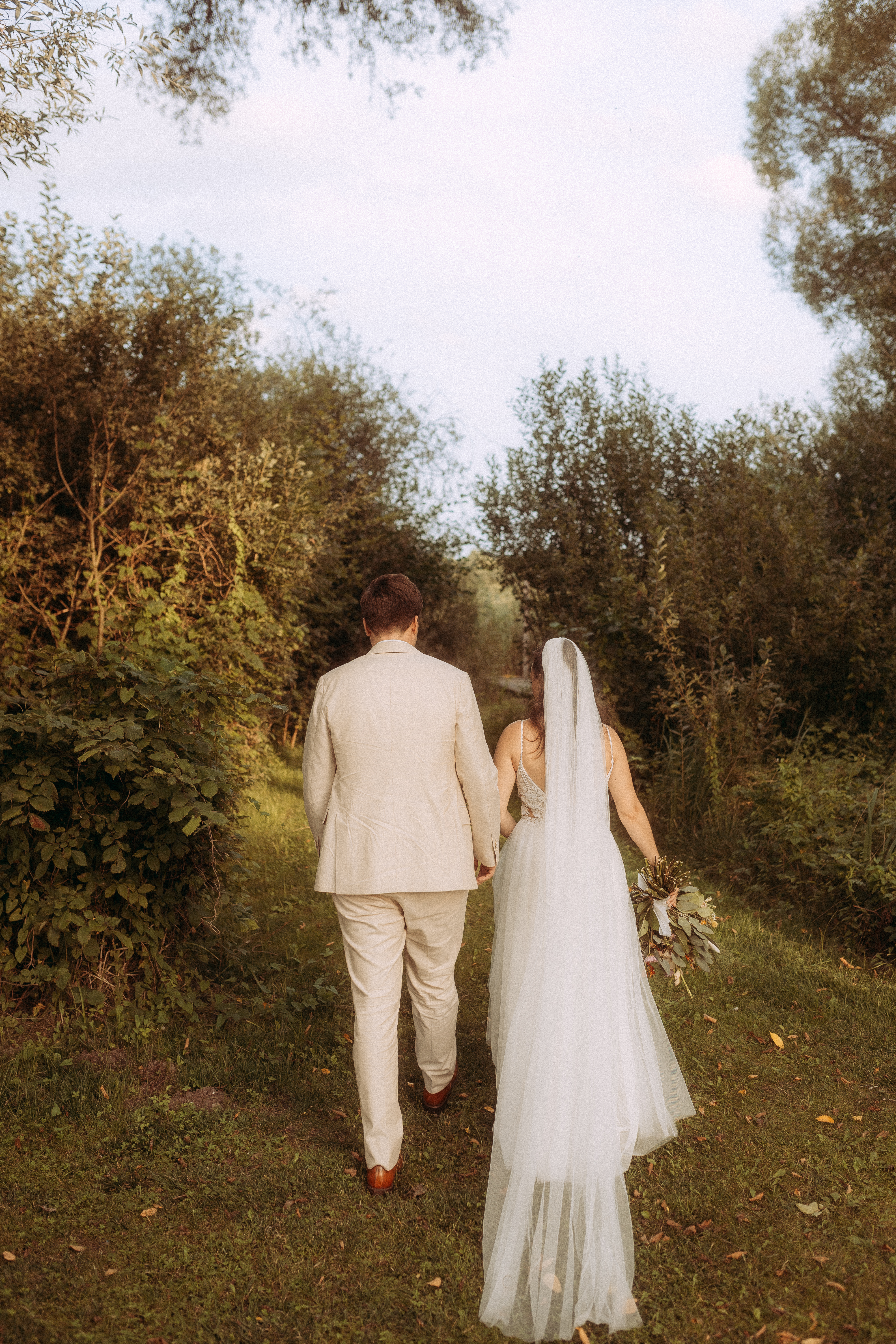 Brautpaar Hand in Hand auf dem Weg zur Hochzeit am Haus Heinz am See.