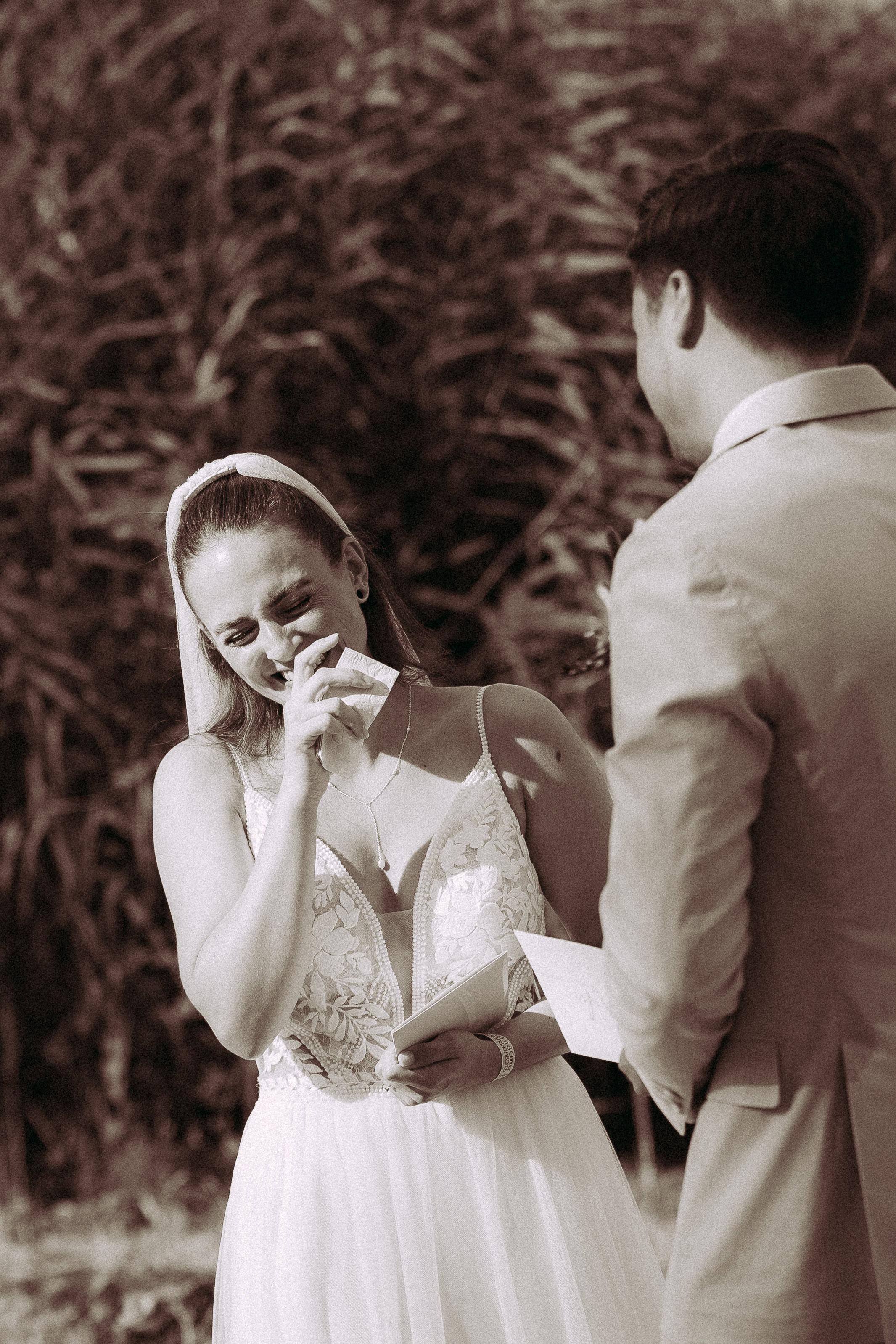 Braut weint gerührt bei der Hochzeit am Haus Heinz am See, während Bräutigam zusieht.