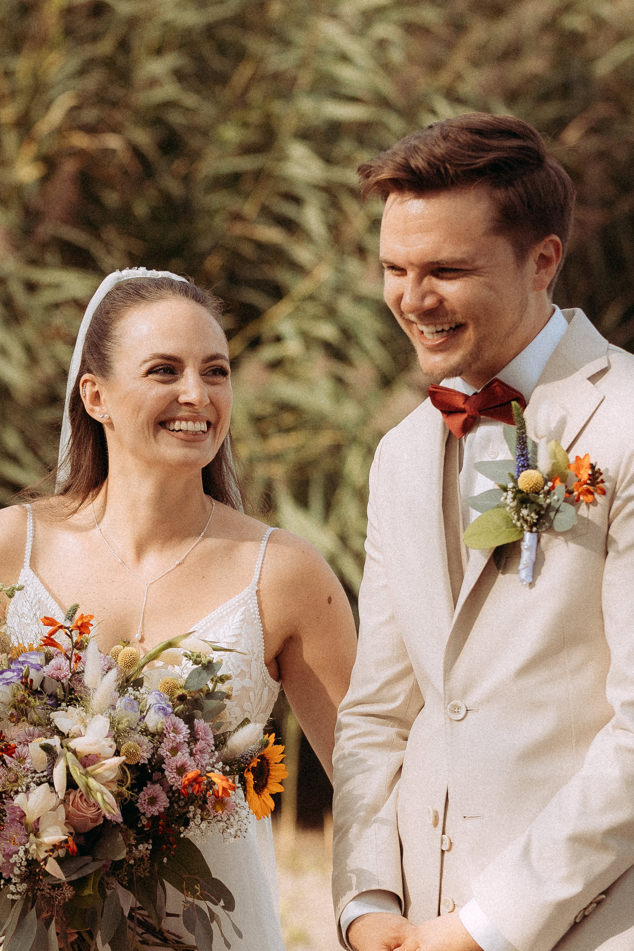 Brautpaar lacht bei Hochzeit am Haus Heinz am See, Blumenstrauß und Anstecker