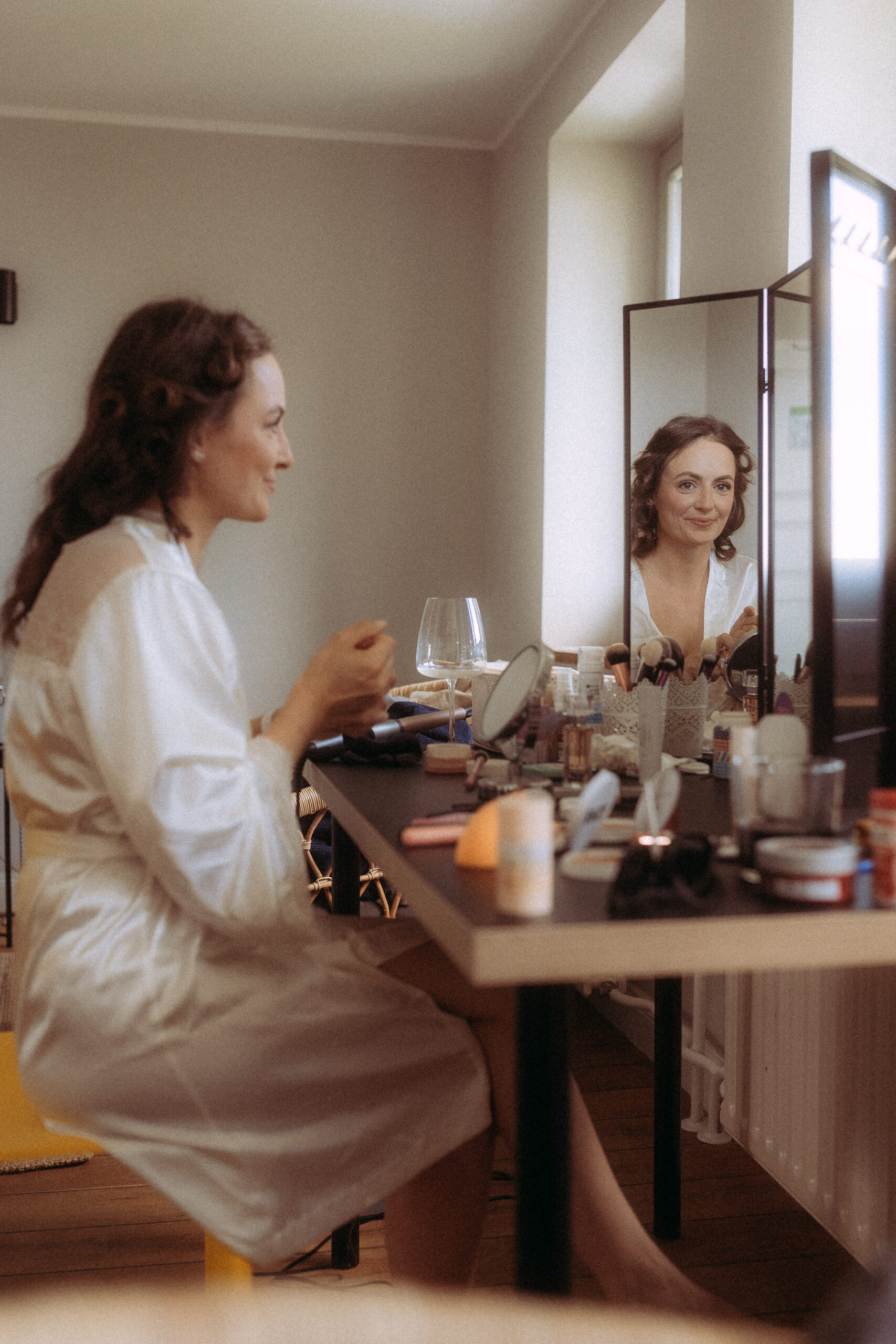 Braut stylt sich vor dem Spiegel am Hochzeitstag, Haus Heinz am See