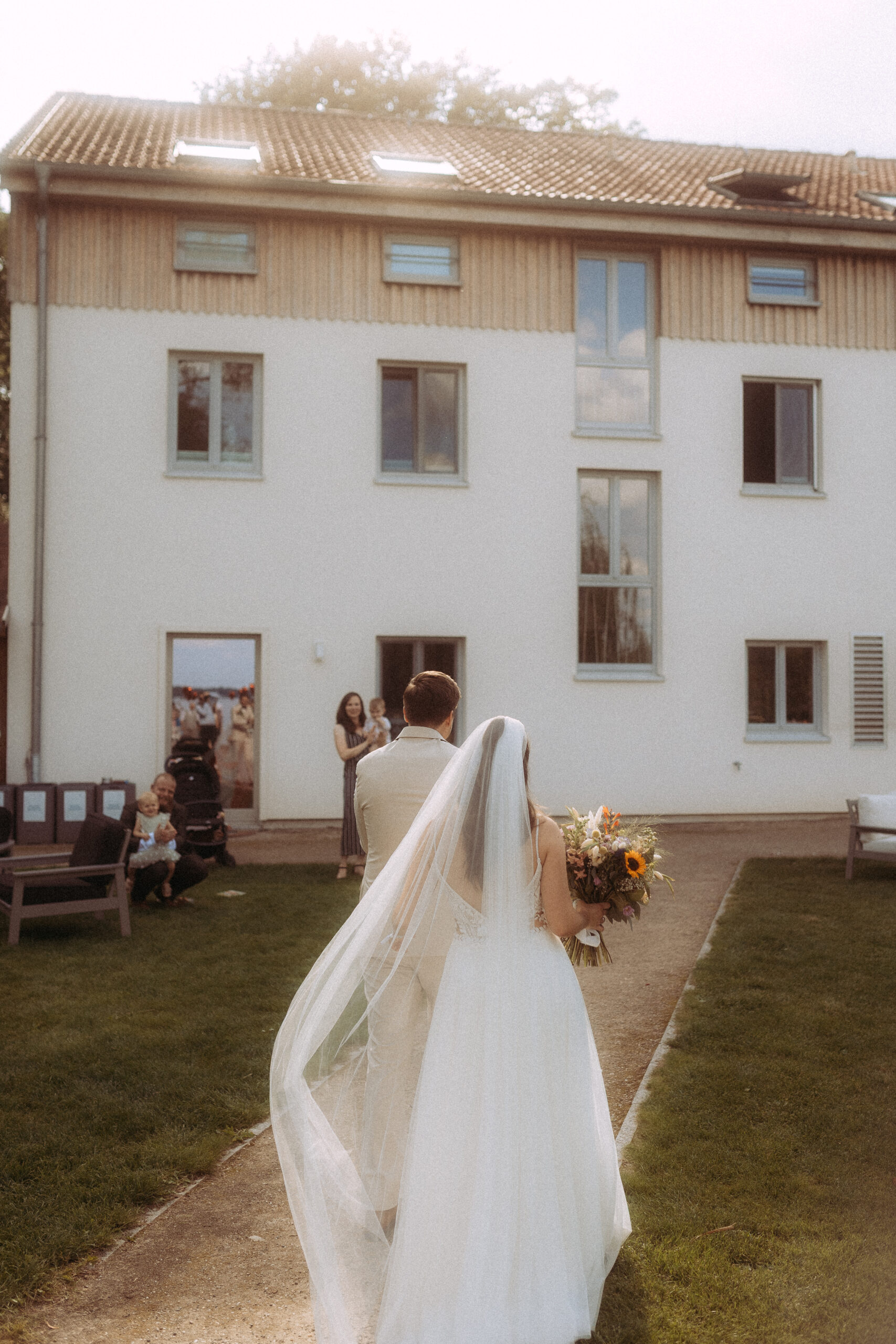 Brautpaar geht auf Gebäude zu, Braut mit Blumenstrauß. Hochzeit Preise.