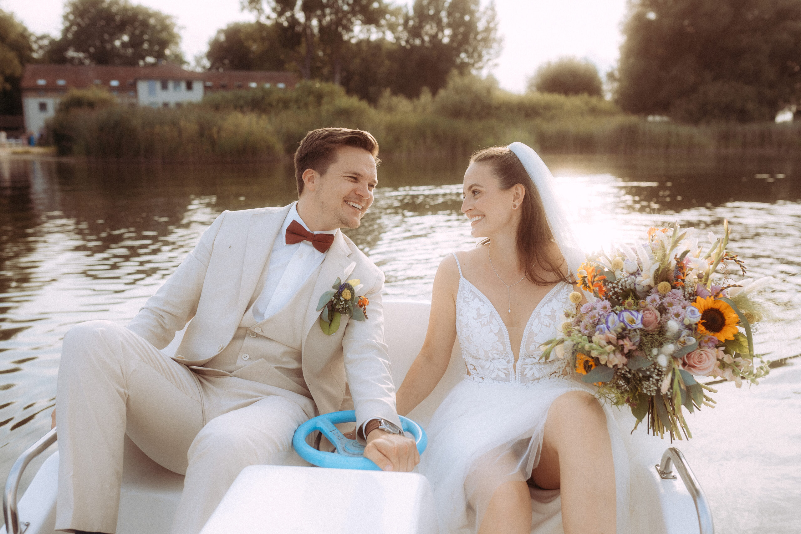 Brautpaar glücklich auf einem Tretboot mit Blumenstrauß und See im Hintergrund
