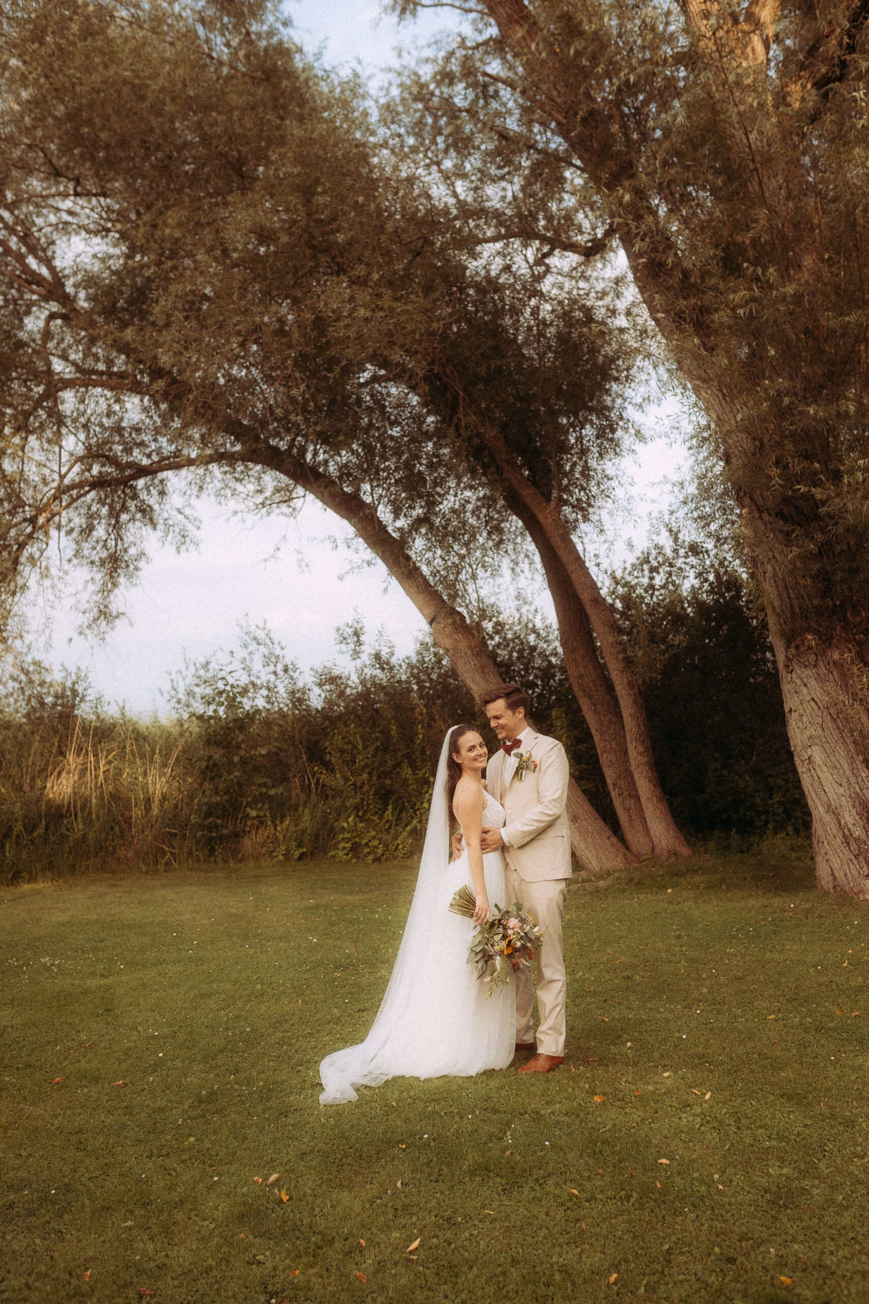 Brautpaar umarmt sich unter einem Baum auf einer Hochzeit im Freien.