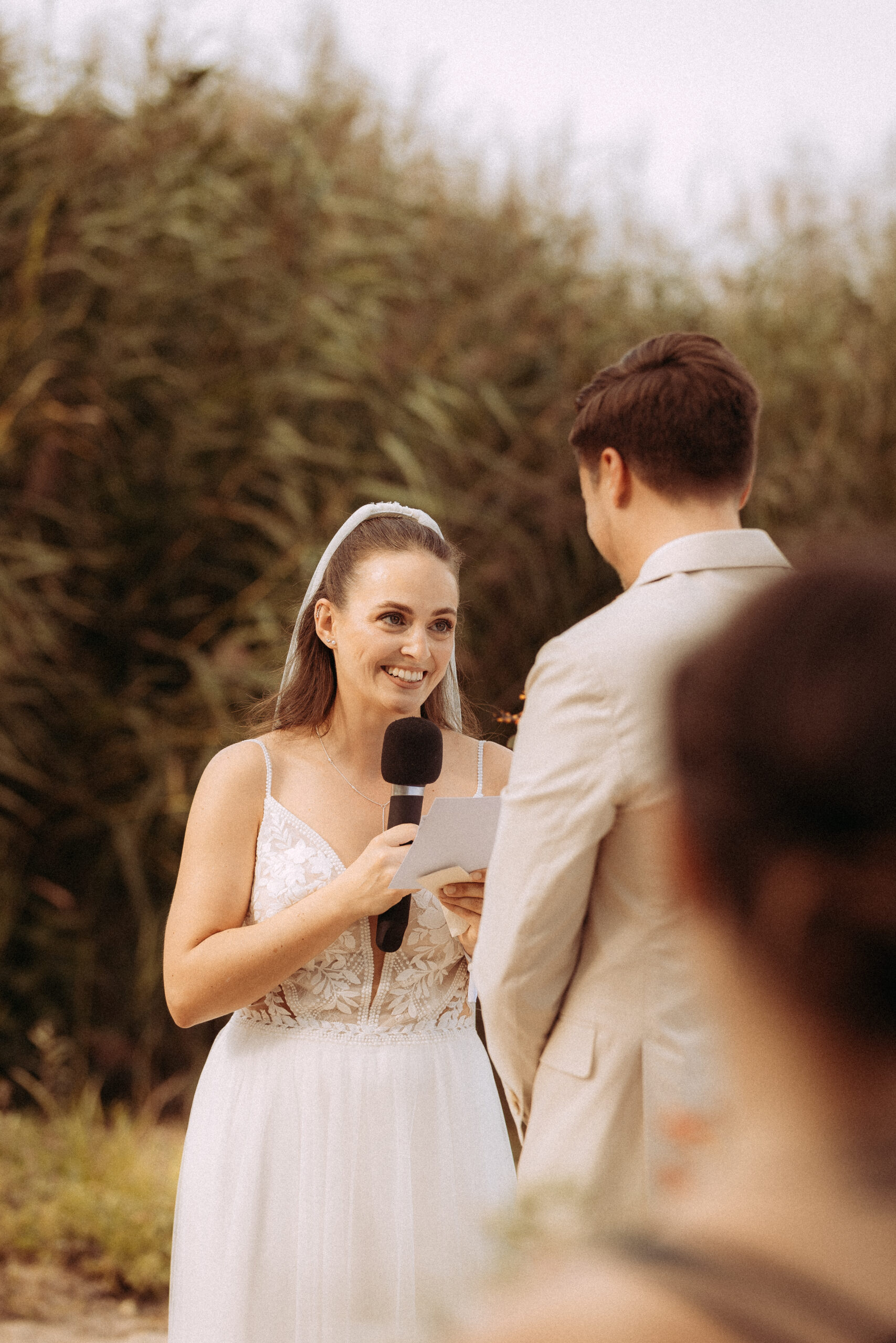 Braut hält Rede bei Hochzeit am Haus Heinz am See, lächelnd mit Mikrofon und Dokument