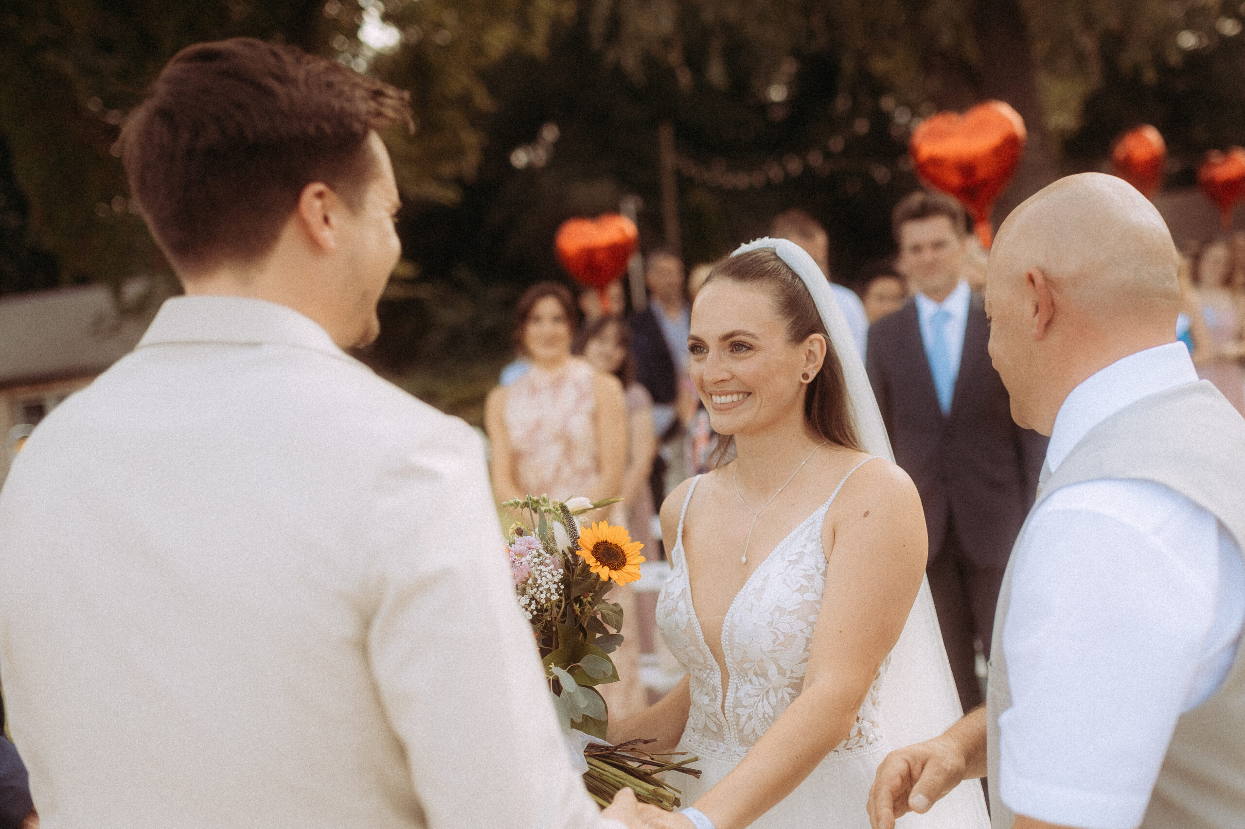 Brautpaar bei Hochzeit am Haus Heinz am See, lächelnde Braut mit Blumenstrauß.