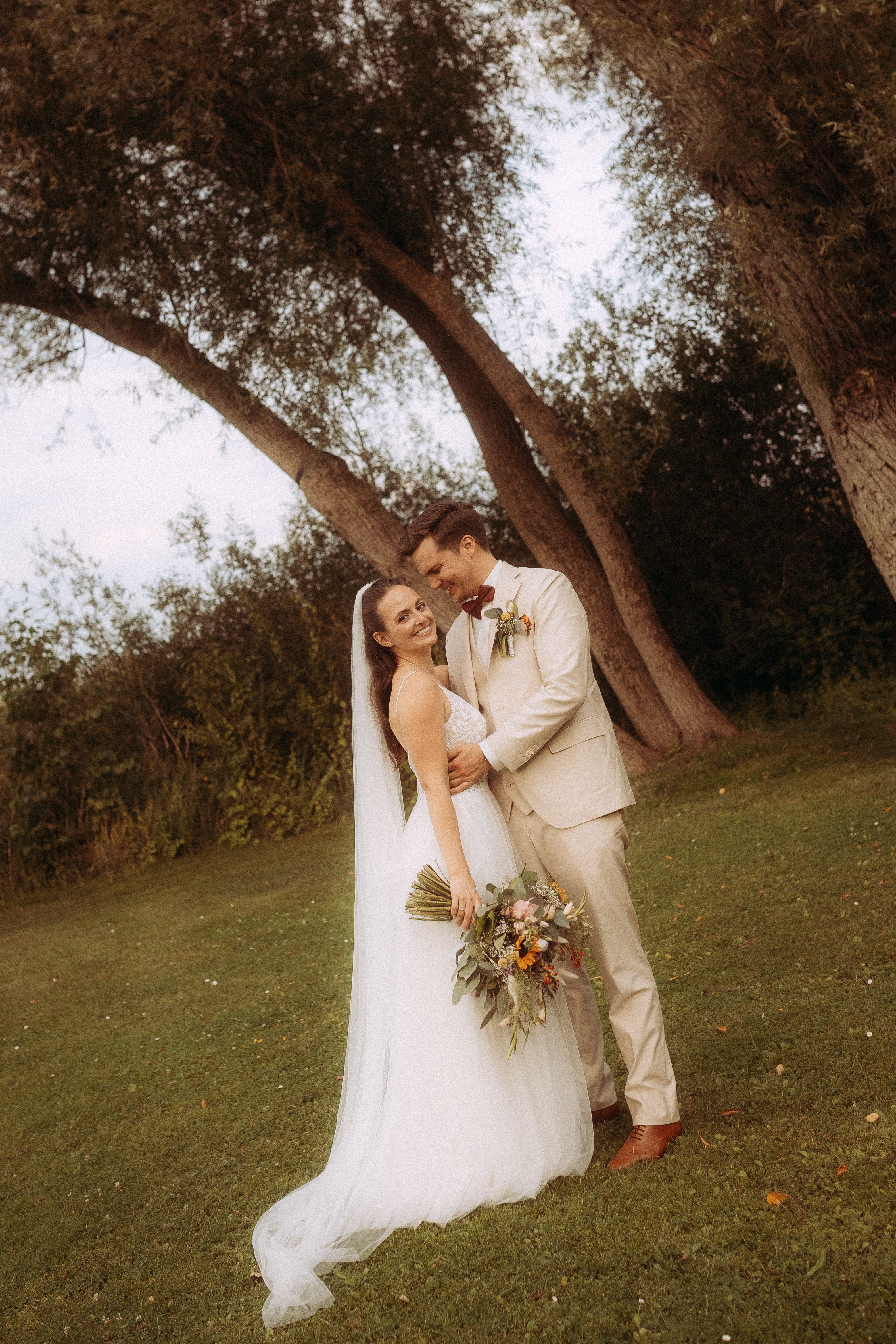 Brautpaar umarmt sich liebevoll am Haus Heinz am See, Hochzeit im Grünen