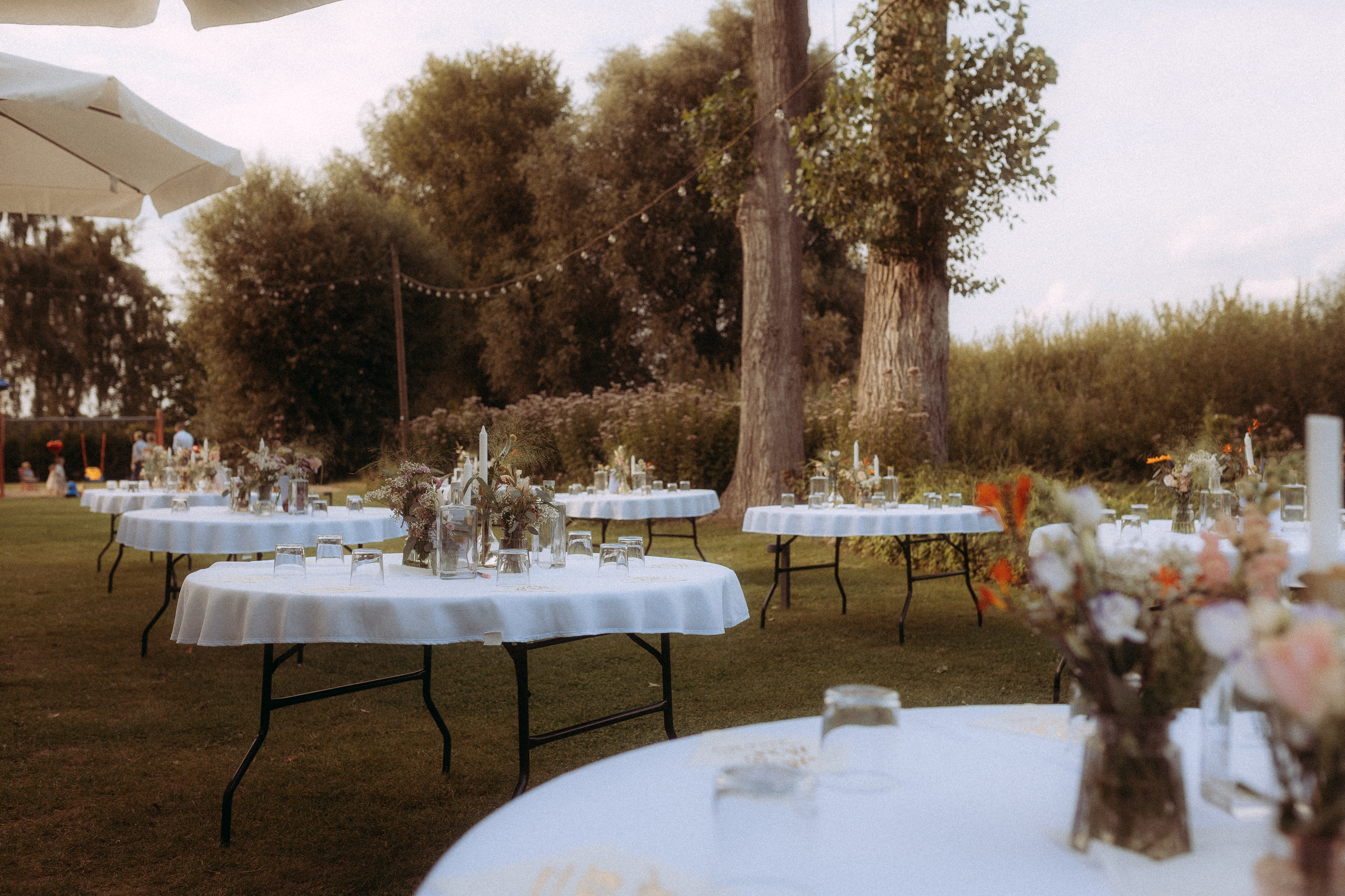 Gedeckte Hochzeitstische im Freien mit Blumenarrangements auf Rasenfläche