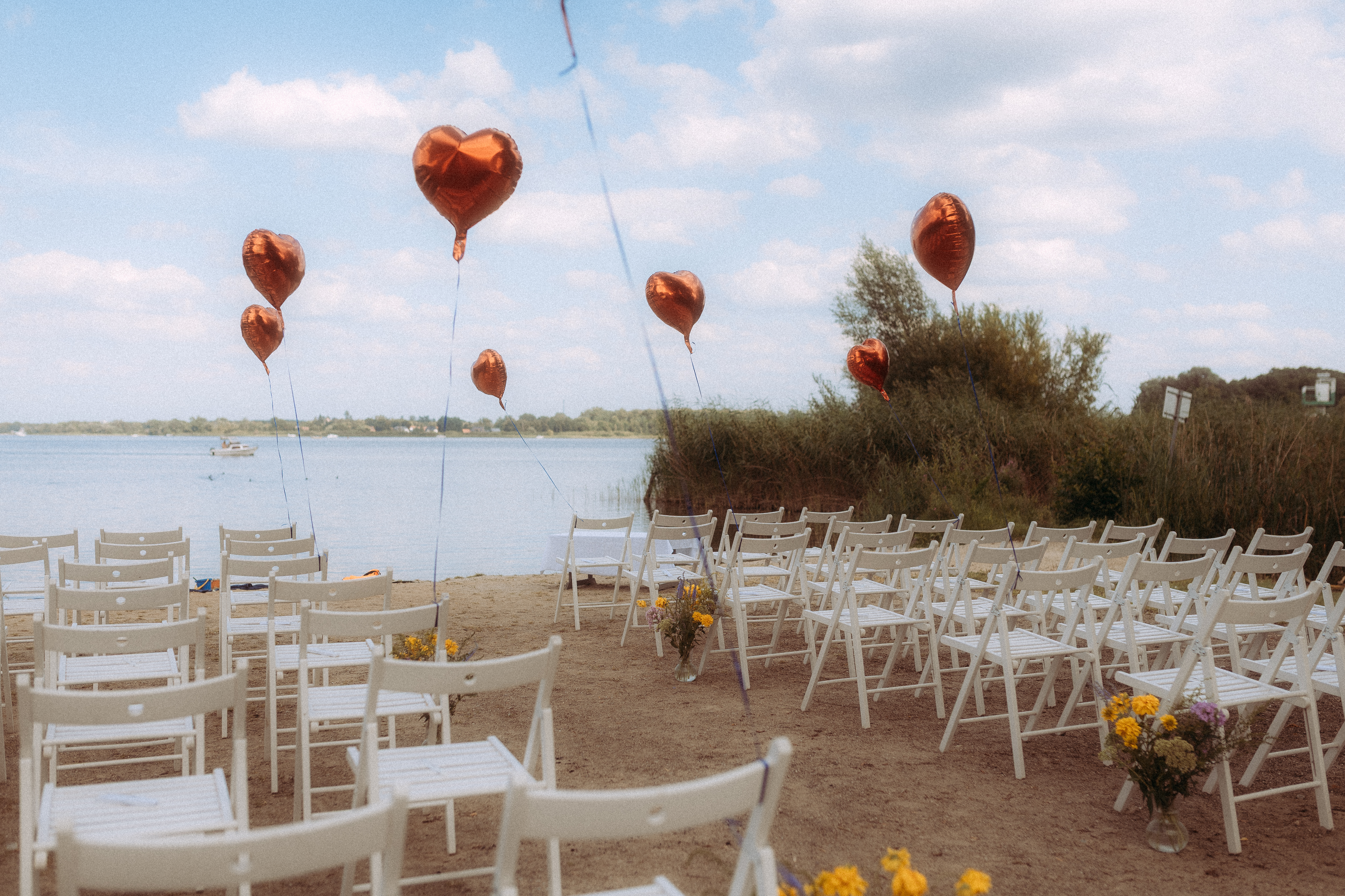 Hochzeitszeremonie am Haus Heinz am See mit weißen Stühlen und Herzballons