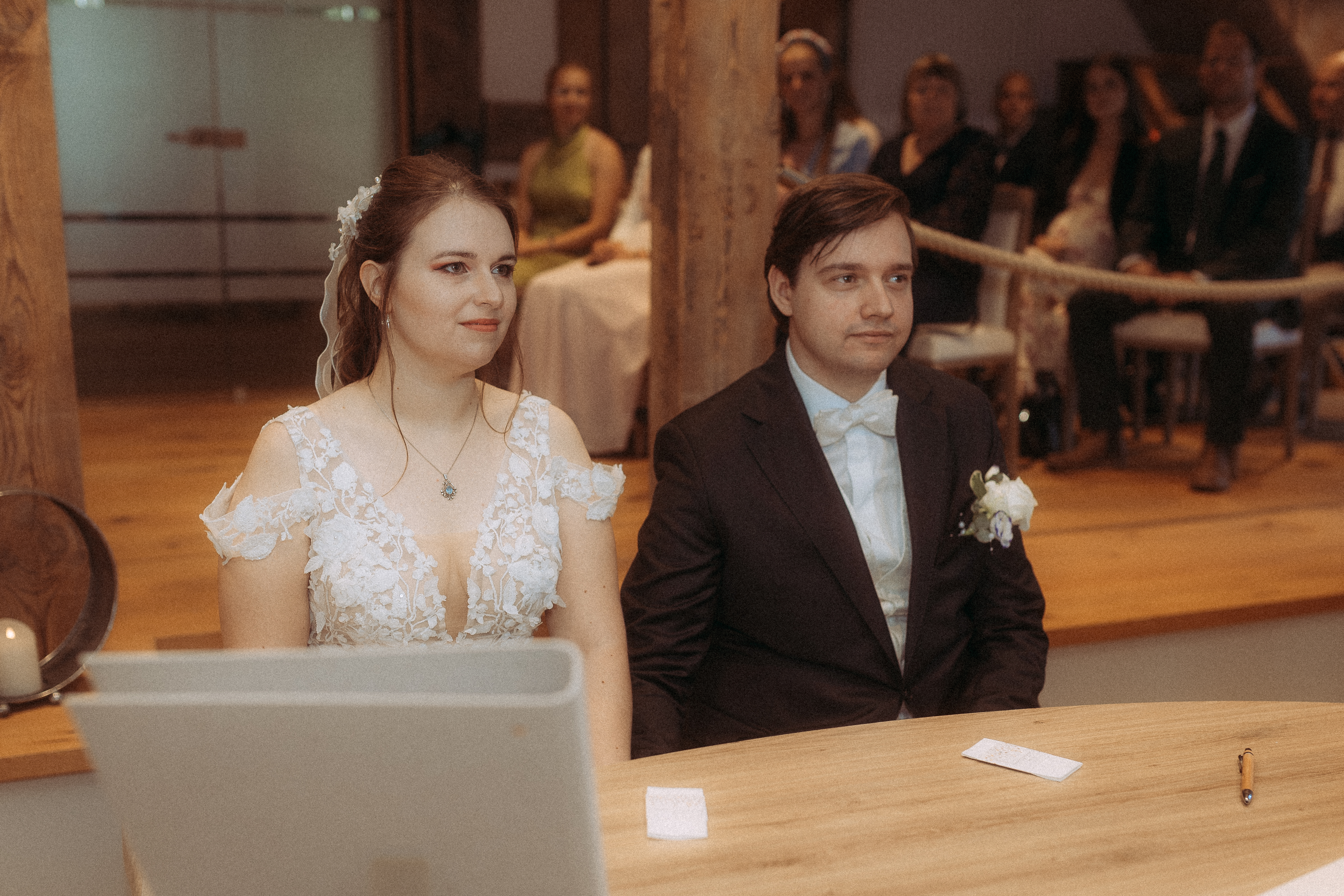 Brautpaar sitzt am Tisch während der Hochzeitszeremonie. Die Braut trägt ein weißes Kleid, der Bräutigam einen Anzug.