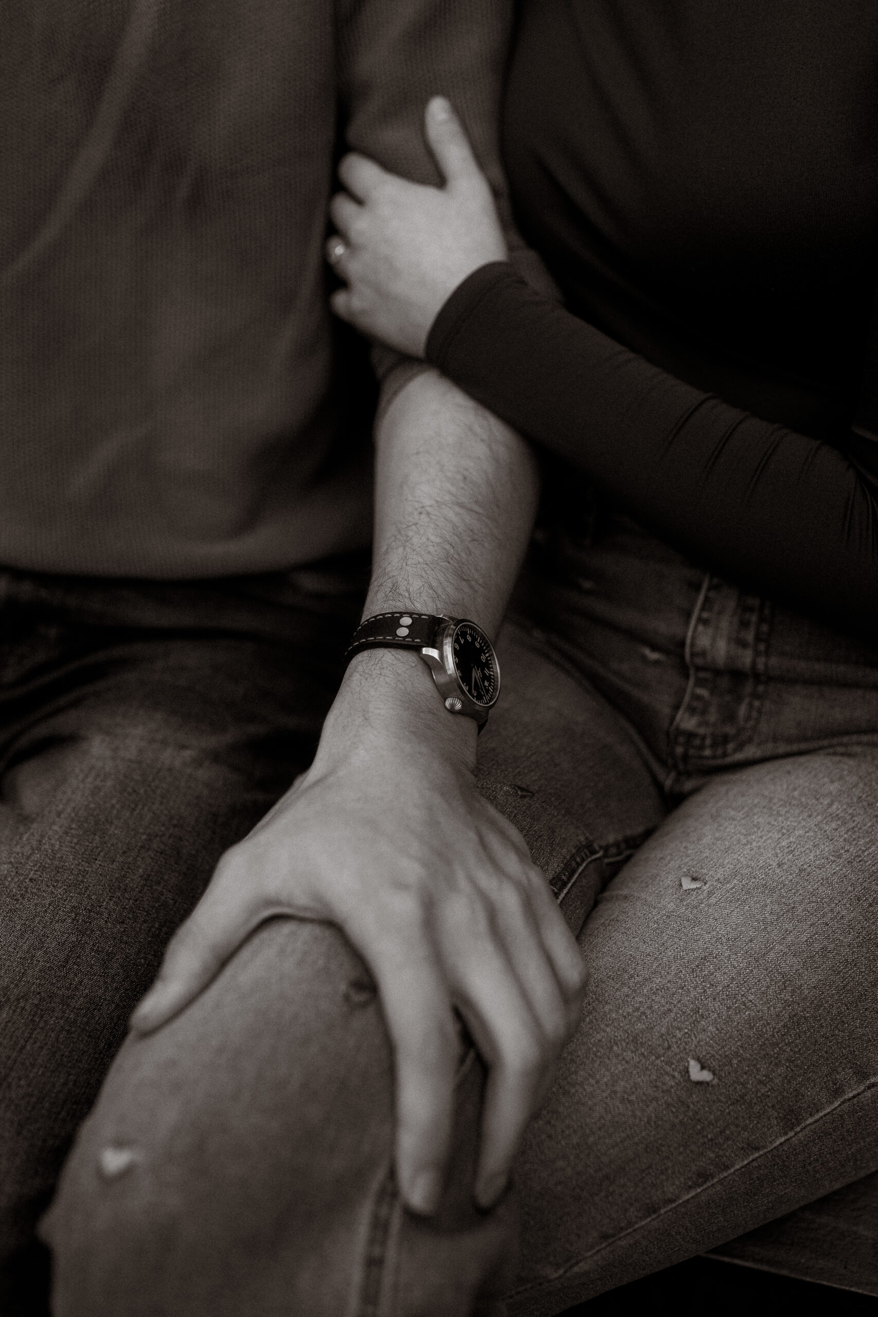 Pärchenshooting Basthorst: Paar sitzt eng umschlungen in Jeans, Armbanduhr sichtbar.