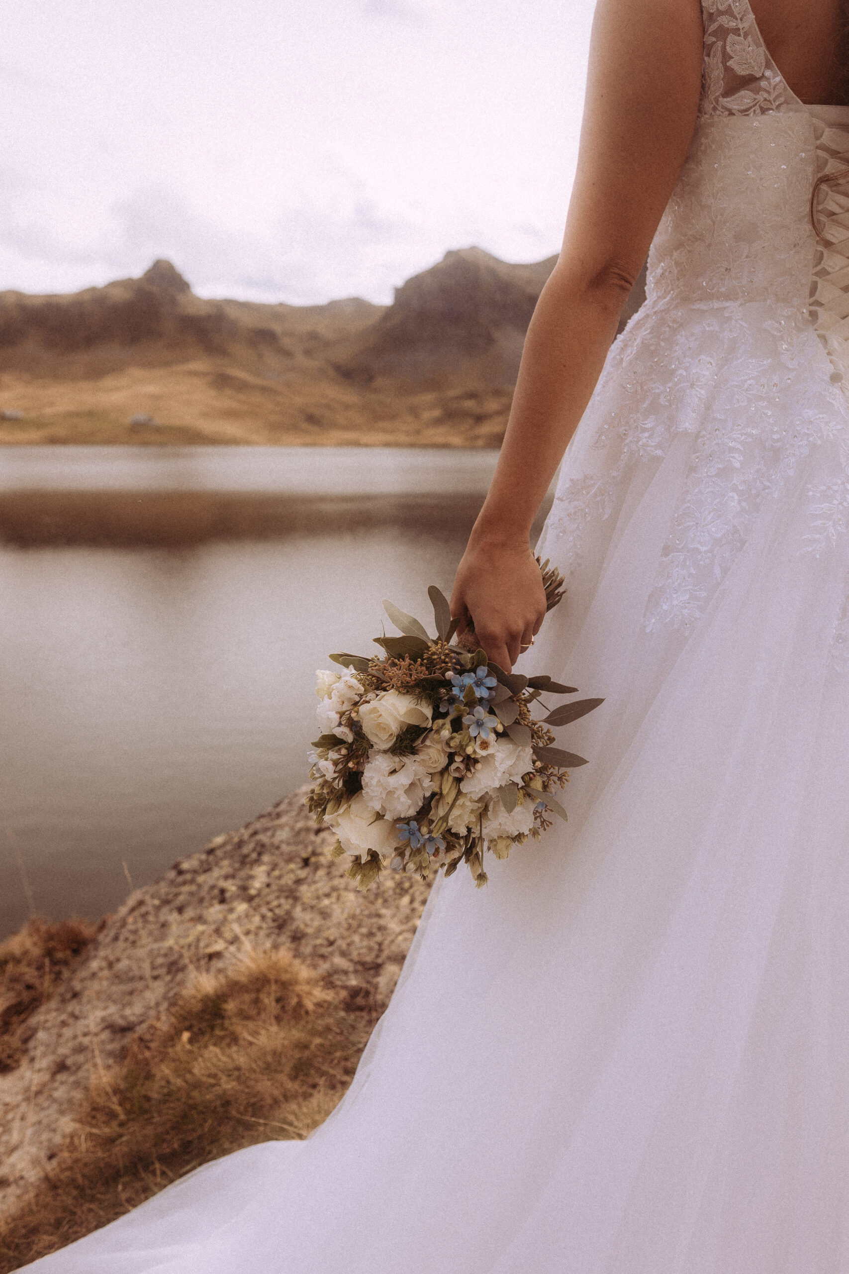 Braut mit Blumenstrauß vor Bergsee. Destination Wedding.