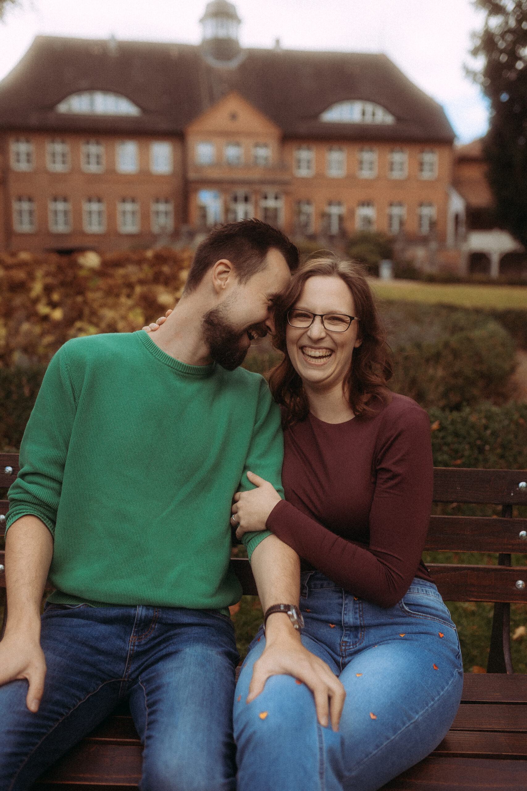 Fröhliches Paar sitzt auf Bank vor großem Haus. Familienfotografie im Freien.