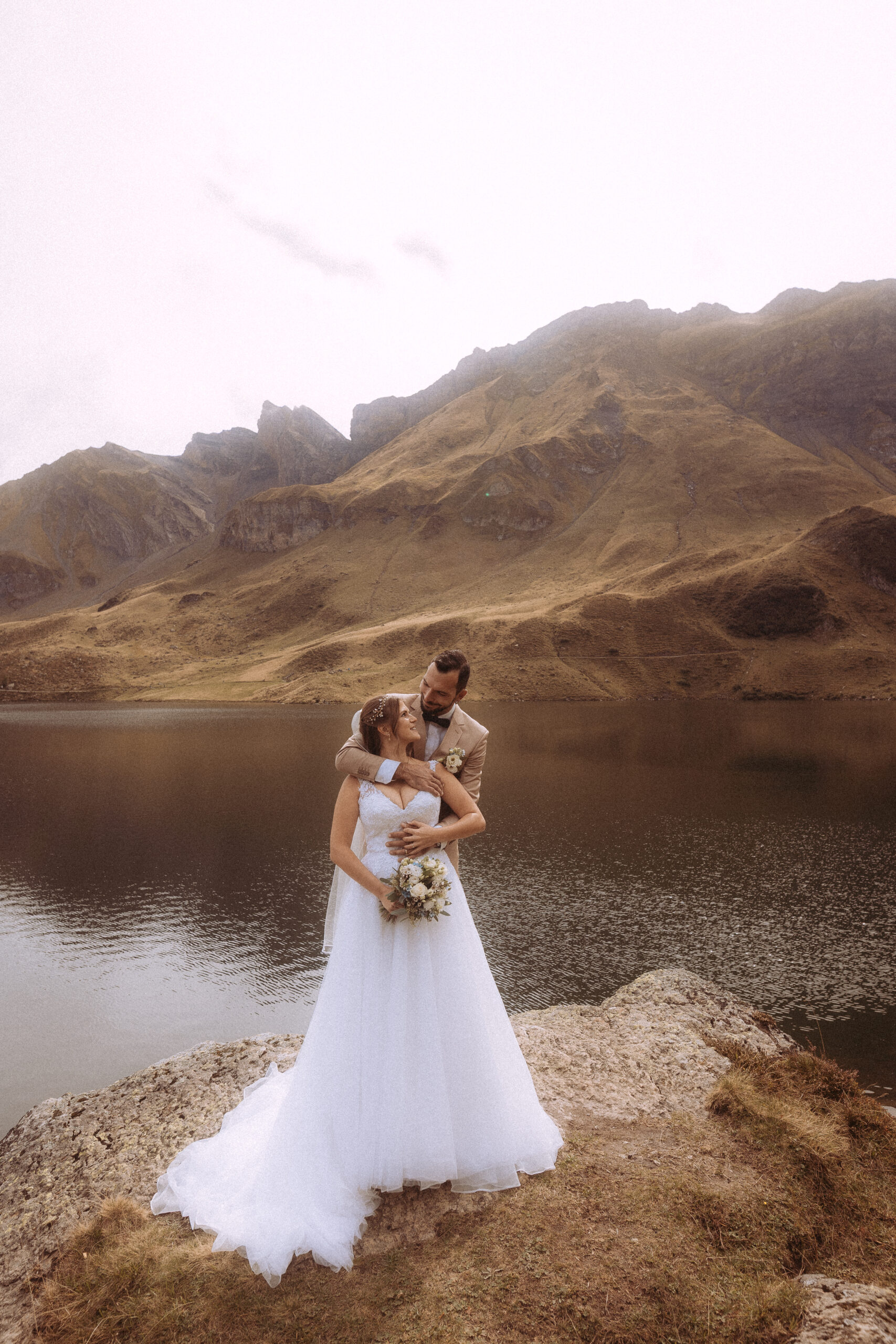 Brautpaar umarmt sich vor Bergsee. Hochzeit in den Bergen.