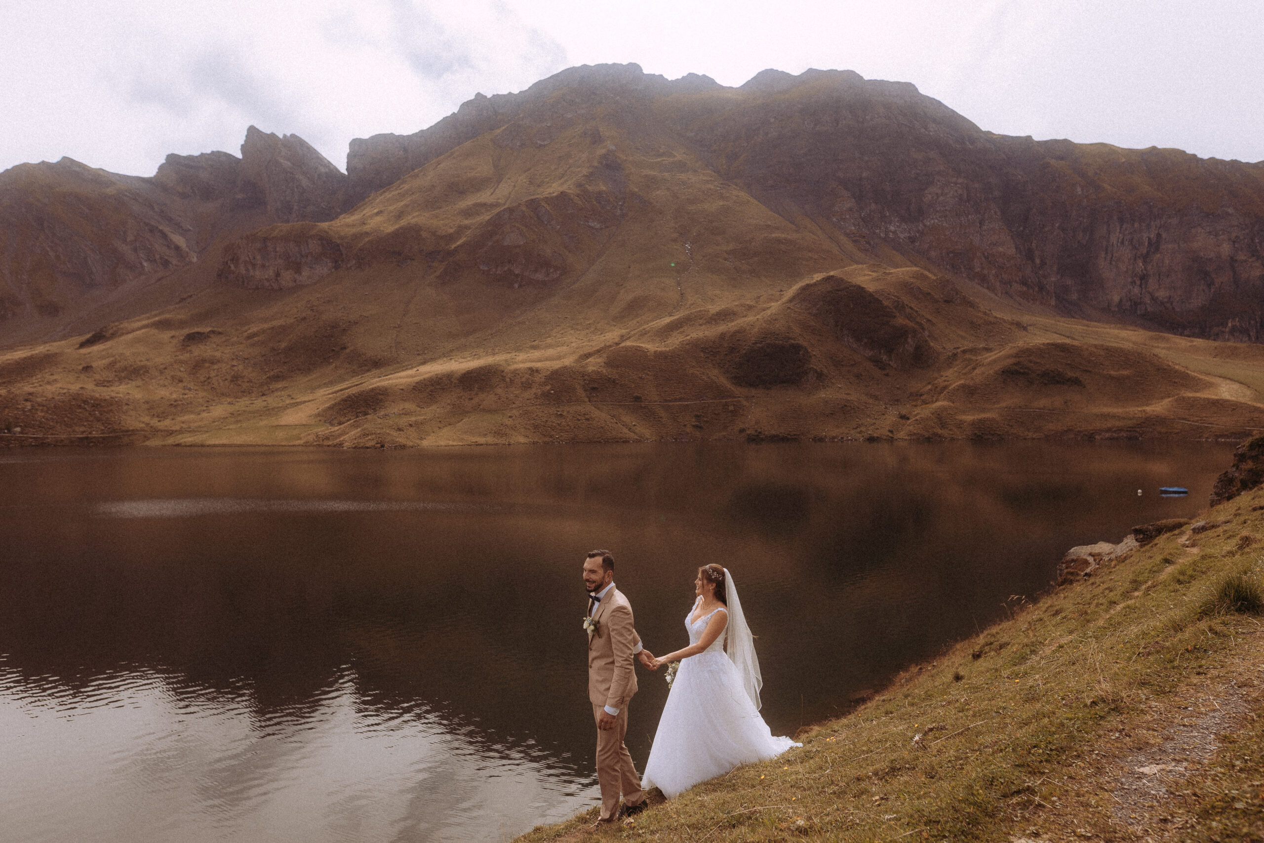 Hochzeitsshooting Melchsee Frutt: Brautpaar Hand in Hand vor Bergsee in der Schweiz