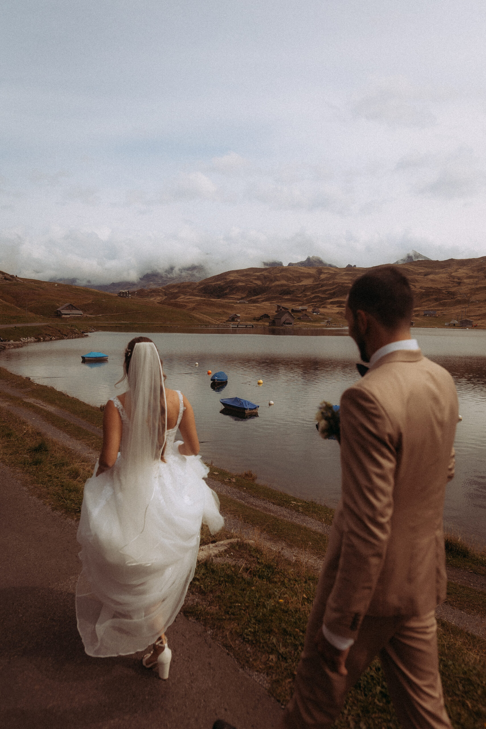 Brautpaar beim Hochzeitsshooting am Melchsee Frutt, Schweiz. Braut im weißen Kleid, See und Berge im Hintergrund.