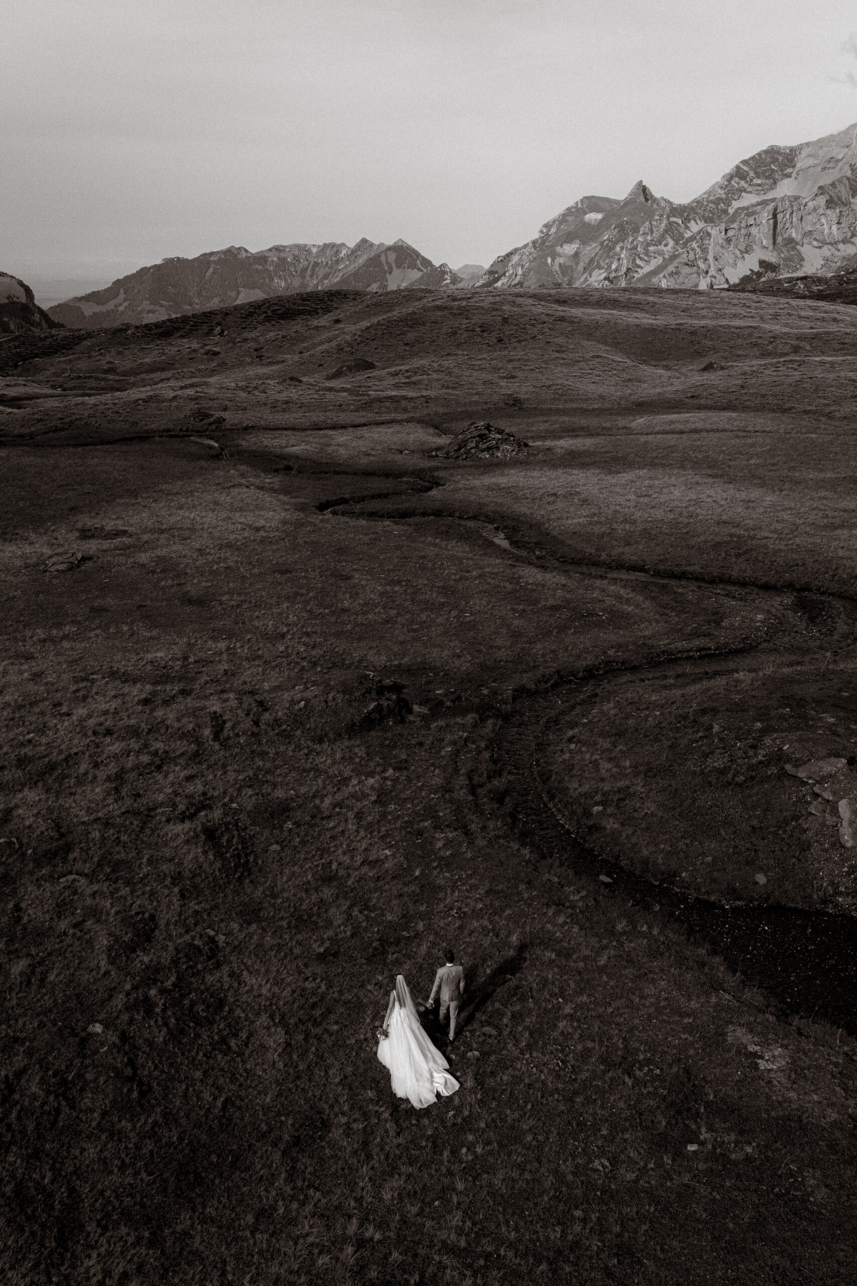 Hochzeitsfoto: Brautpaar wandert in dramatischer Berglandschaft.