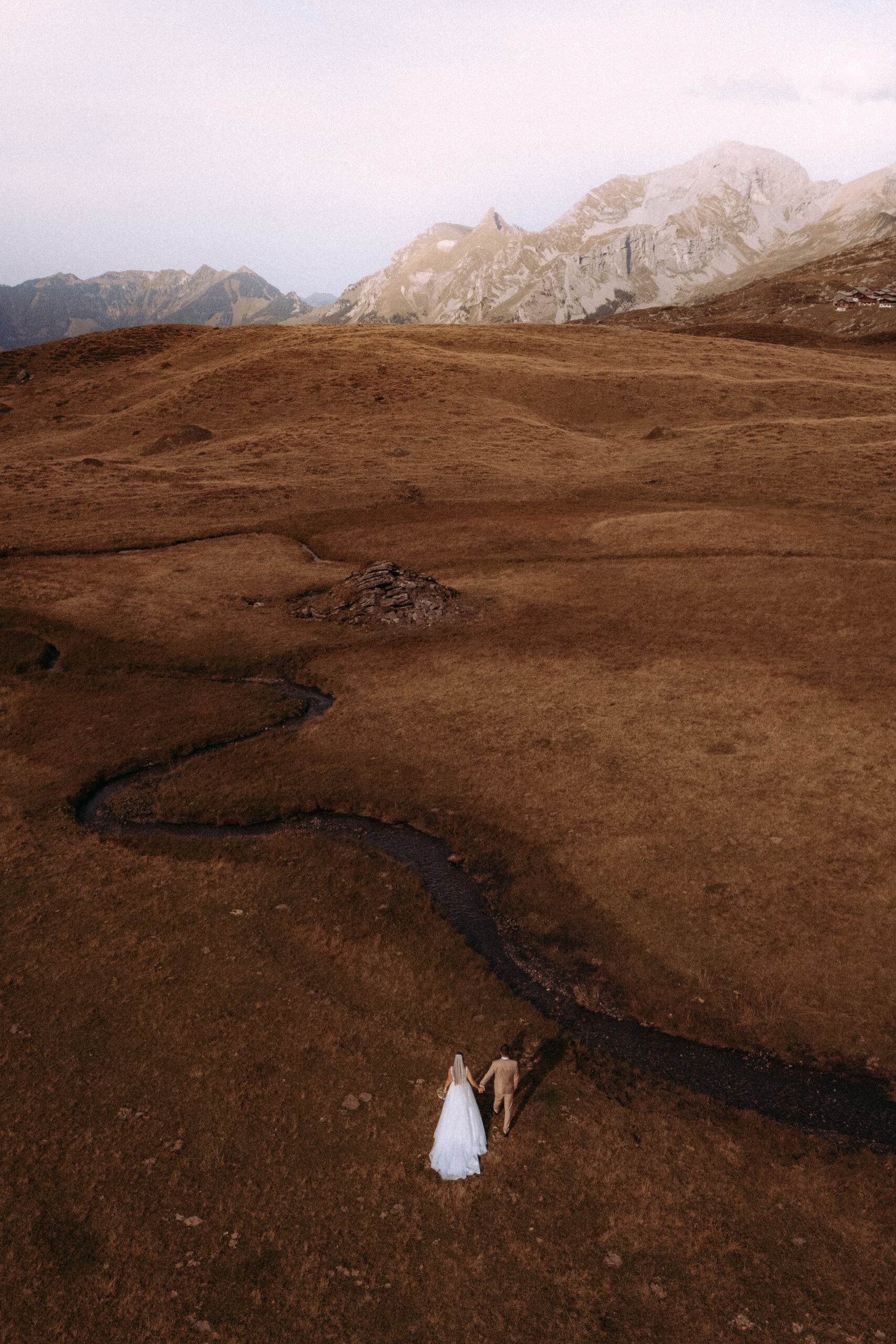 Brautpaar Hand in Hand in Berglandschaft mit Bach. Hochzeit im Freien.