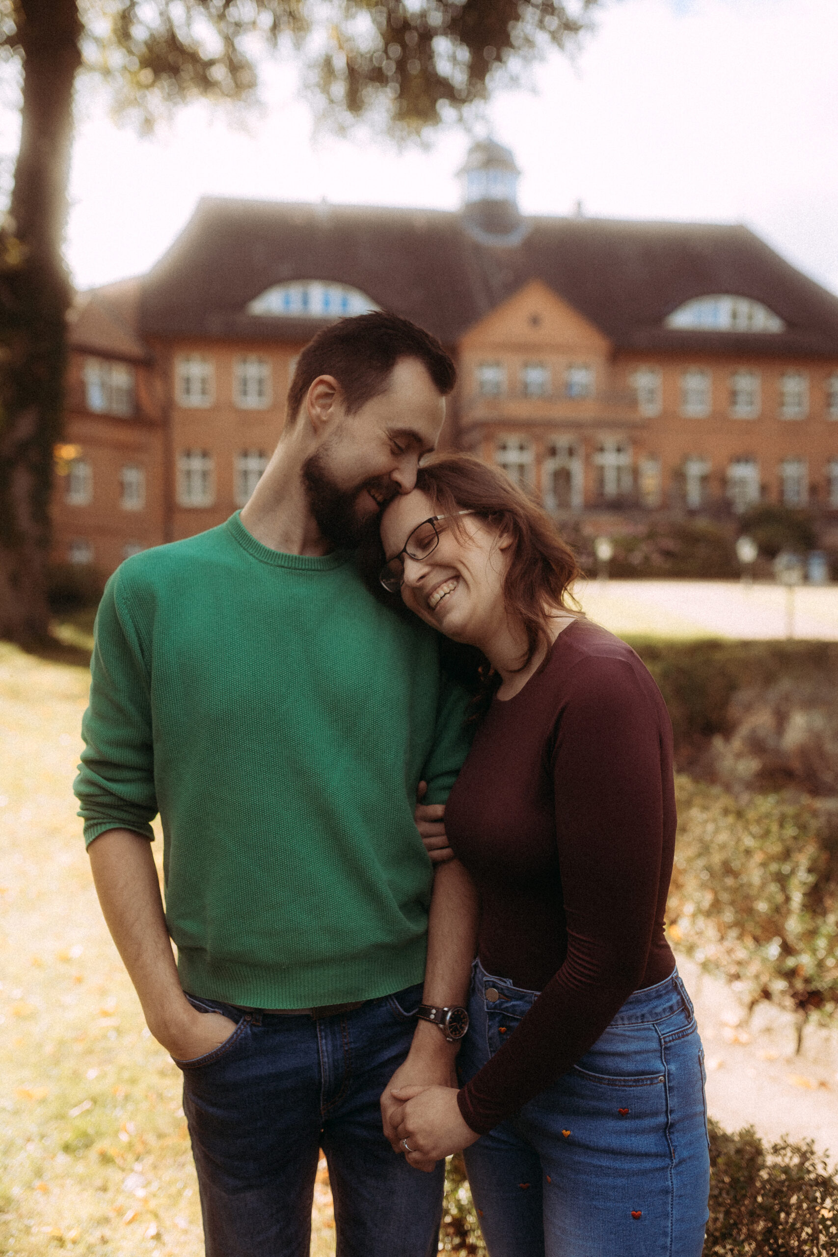 Pärchenshooting in Basthorst: Glückliches Paar umarmt sich vor Backsteingebäude.