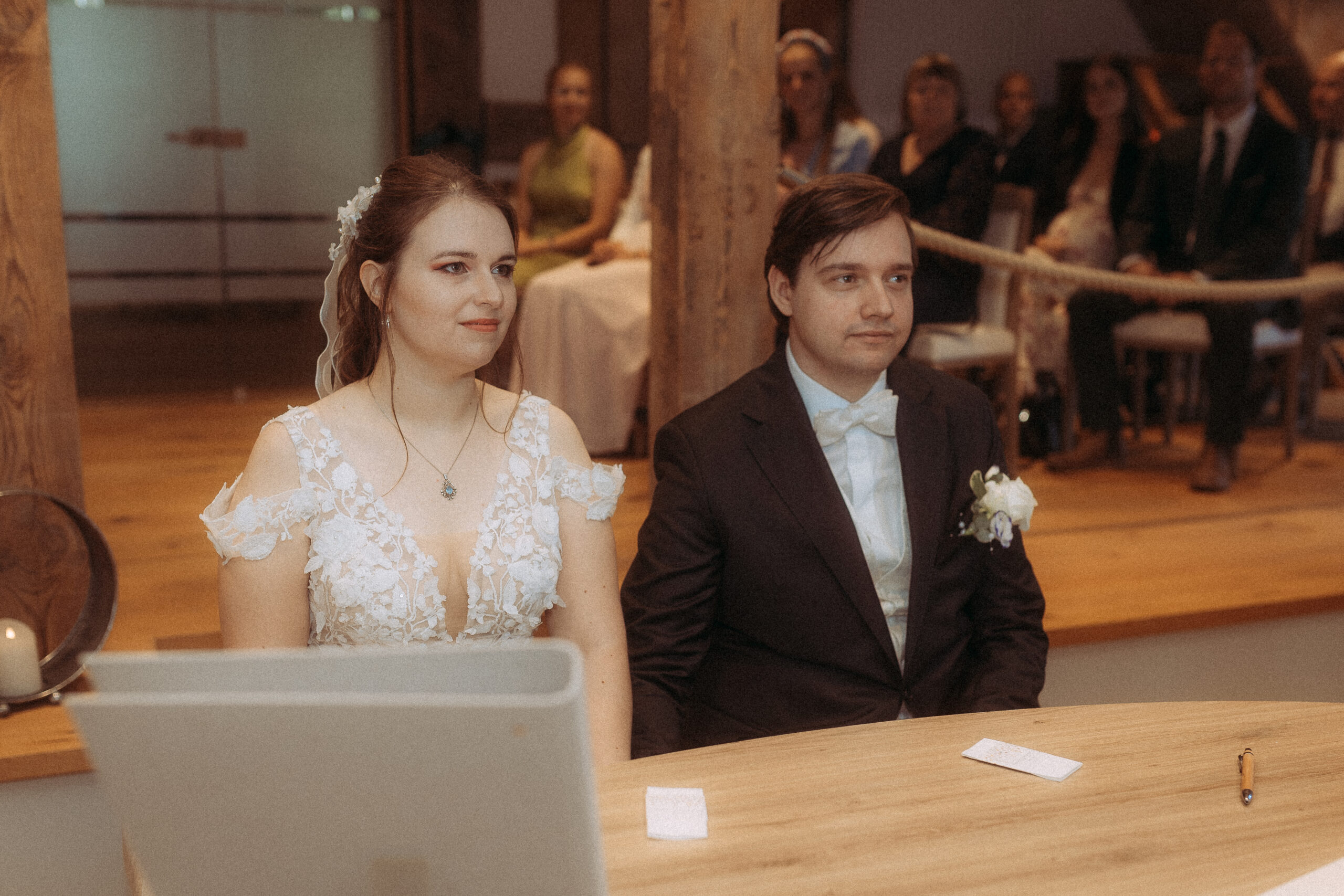 Brautpaar sitzt am Tisch während der Hochzeitszeremonie. Die Braut trägt ein weißes Kleid, der Bräutigam einen Anzug.