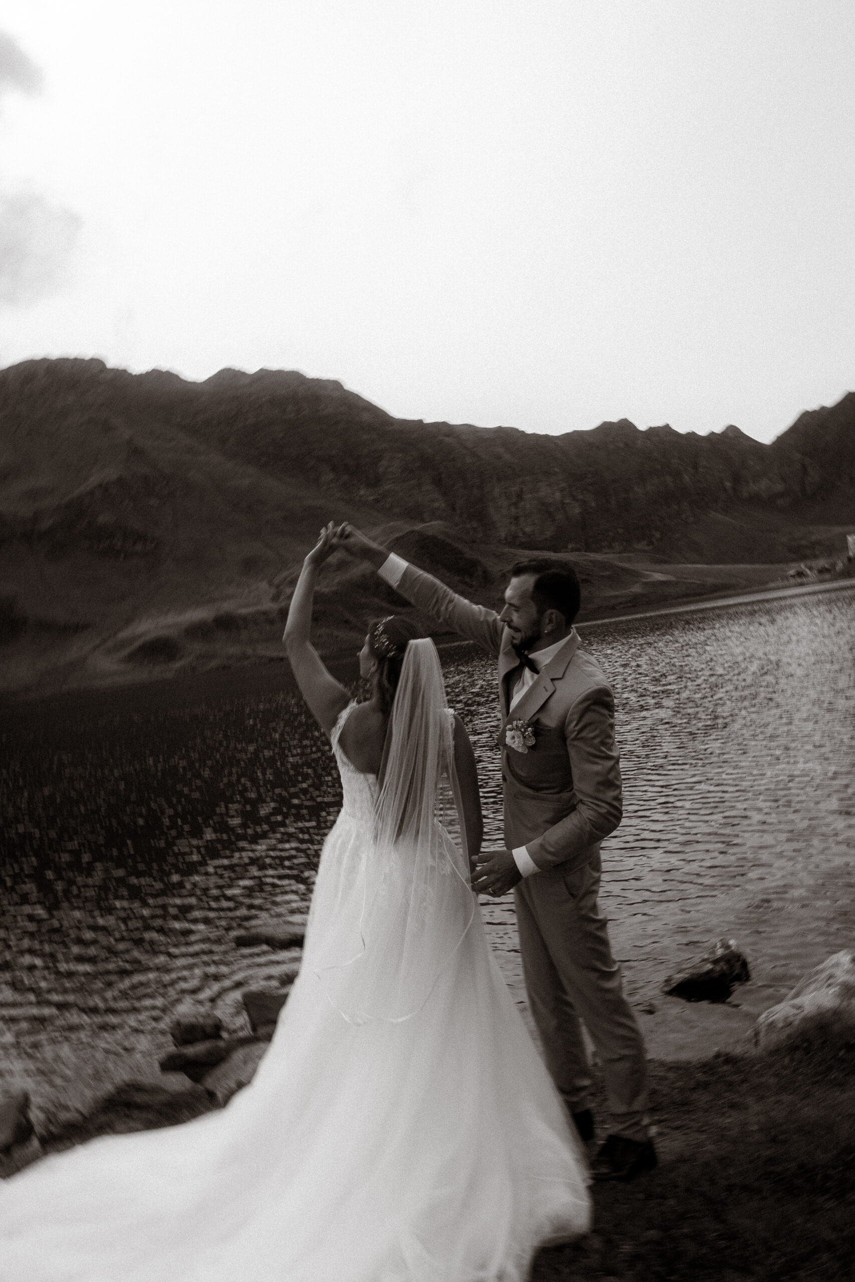 Brautpaar tanzt am See vor Bergkulisse. Hochzeit im Freien.