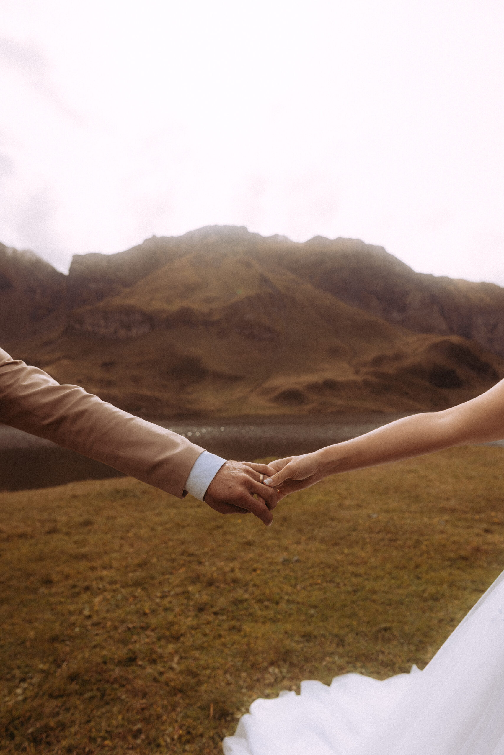 Brautpaar hält Hände bei Hochzeitshooting Melchsee Frutt Schweiz vor Bergkulisse