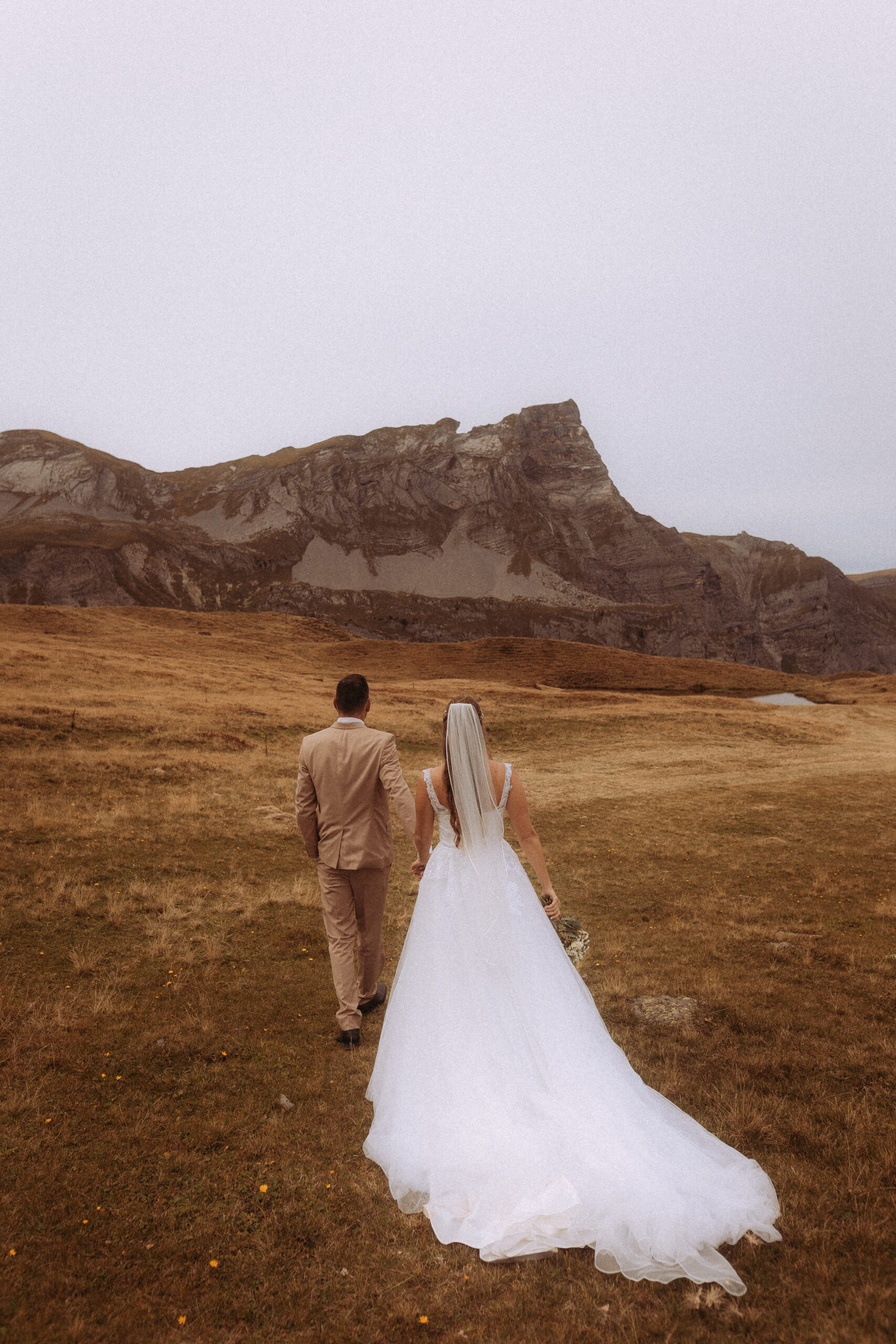 Hochzeitsshooting Melchsee Frutt: Brautpaar wandert vor Bergkulisse.