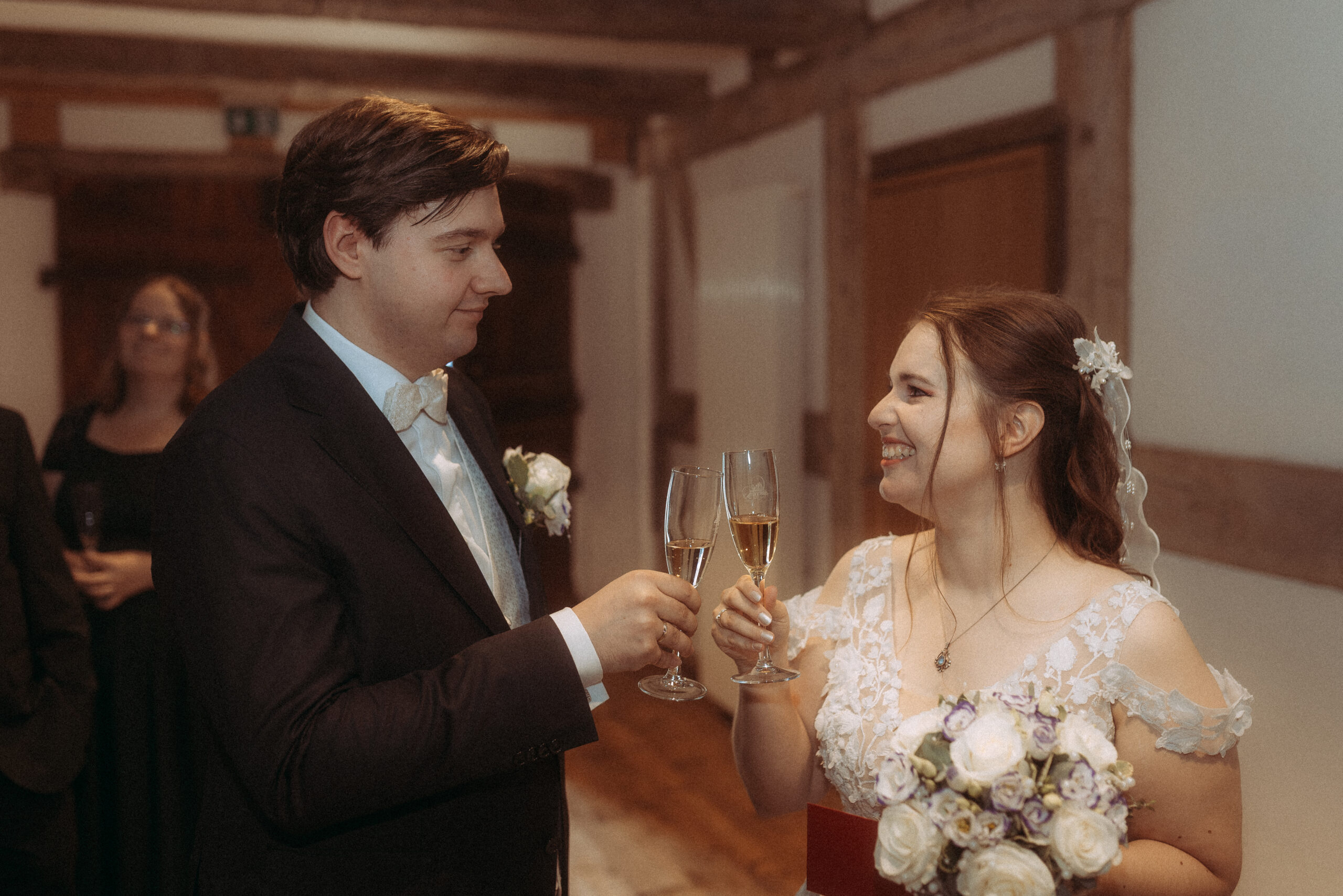 Brautpaar stößt mit Sektgläsern an, glücklich lächelnd. Hochzeit in festlicher Atmosphäre.