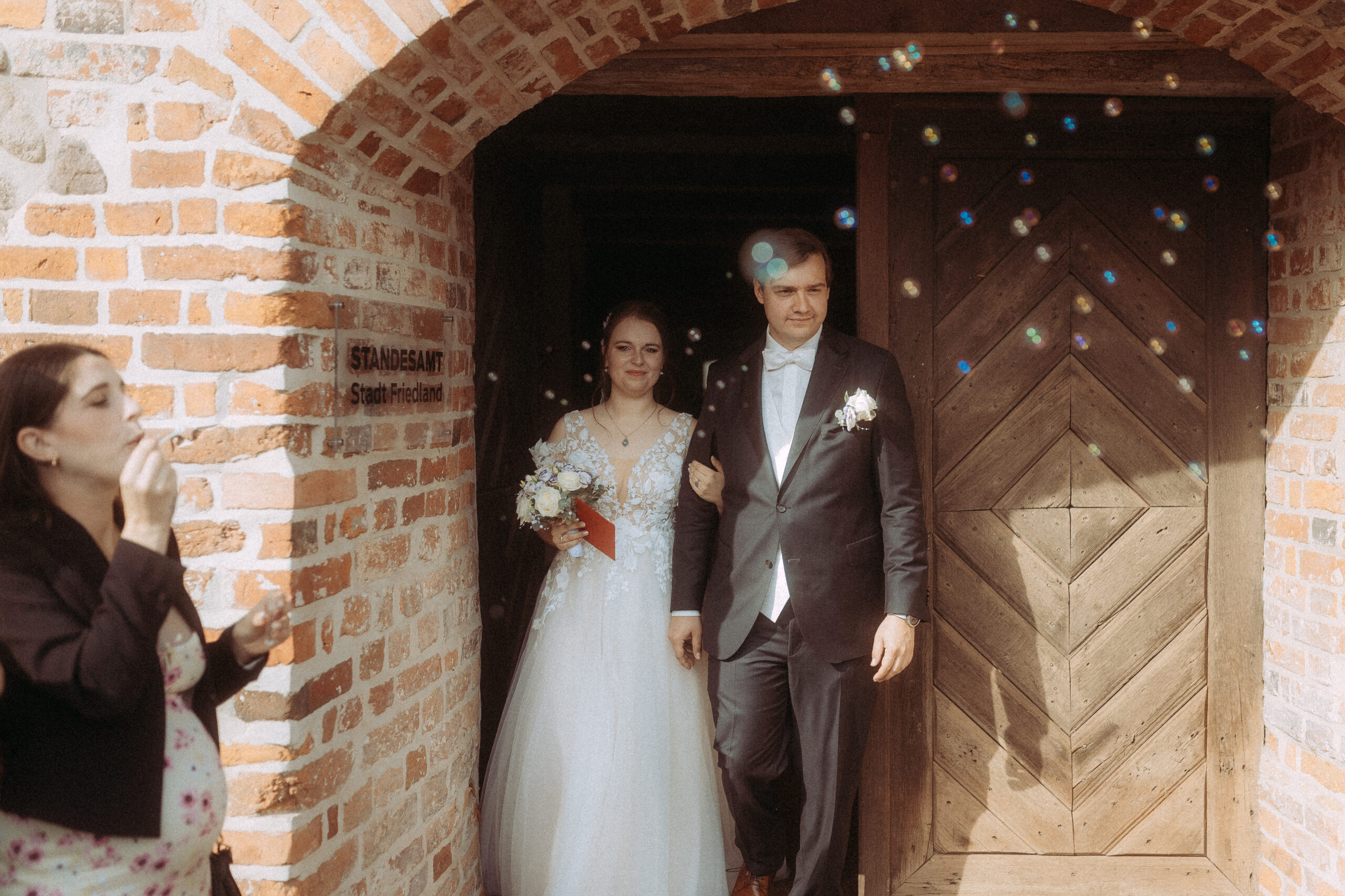 Brautpaar verlässt Standesamt Friedland, umgeben von Seifenblasen. Hochzeit im Backsteingebäude.