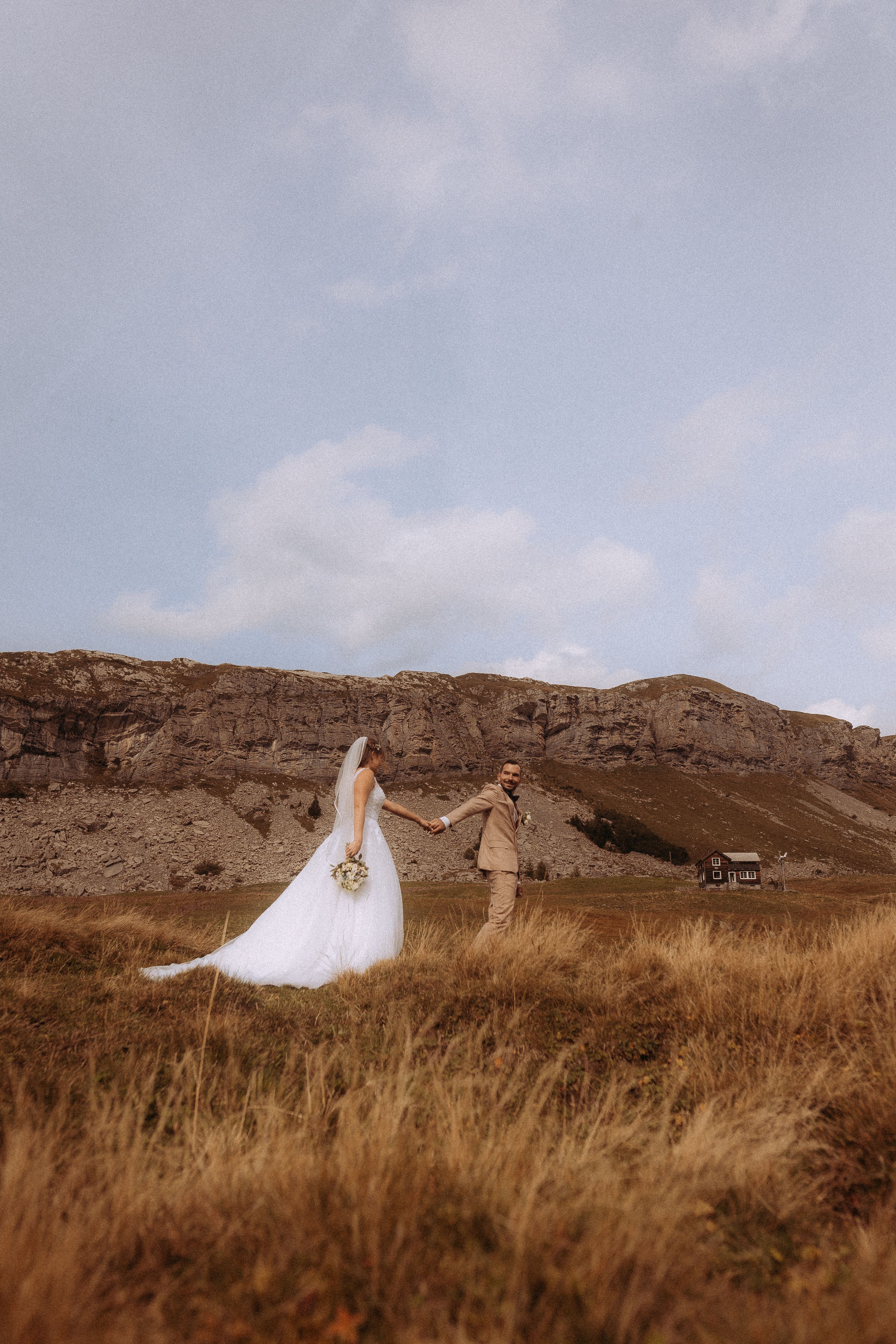 Brautpaar hält Händchen vor Bergkulisse. Destination Wedding im Freien.