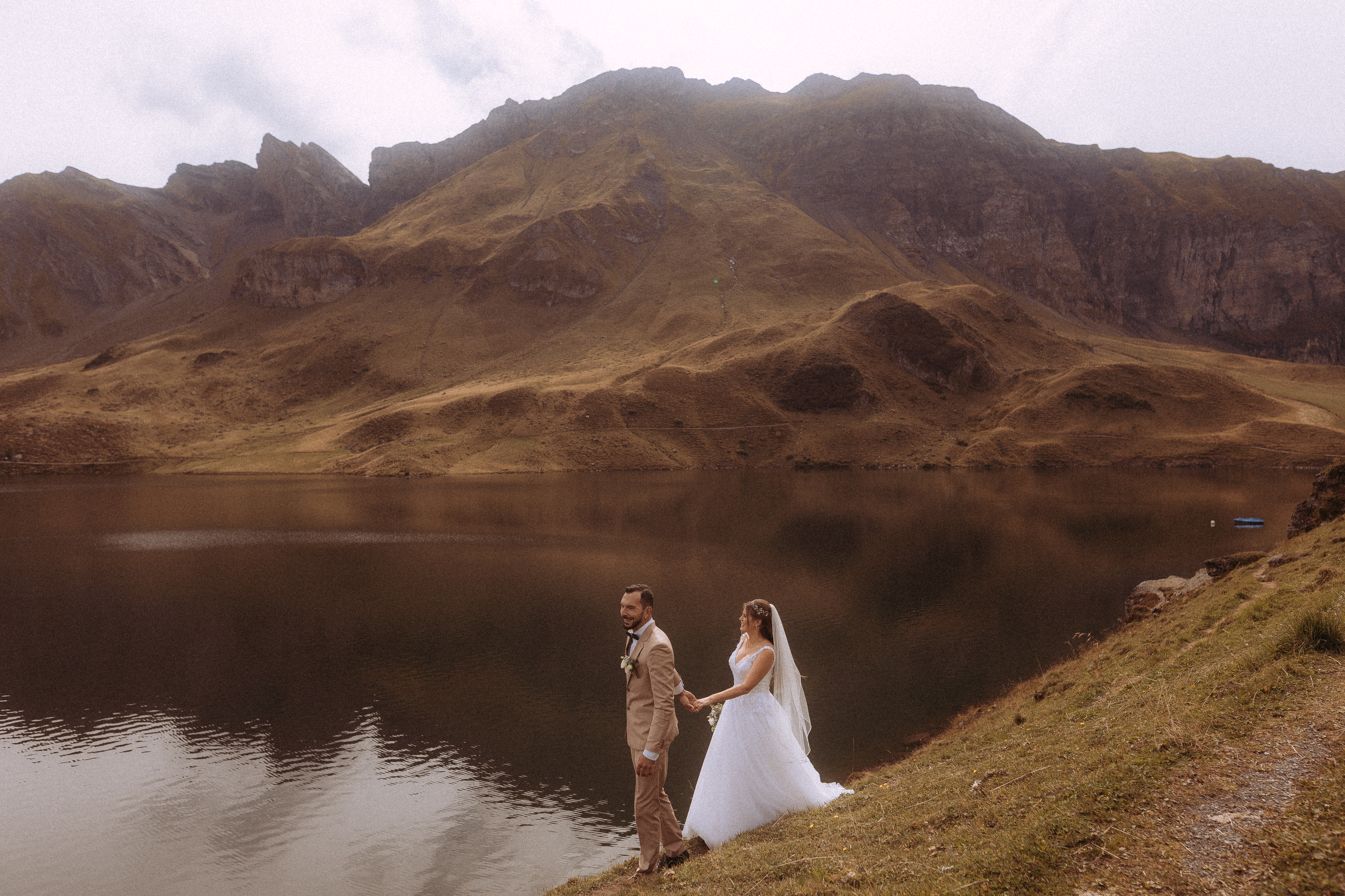 Hochzeitsshooting Melchsee Frutt: Brautpaar Hand in Hand vor Bergsee in der Schweiz