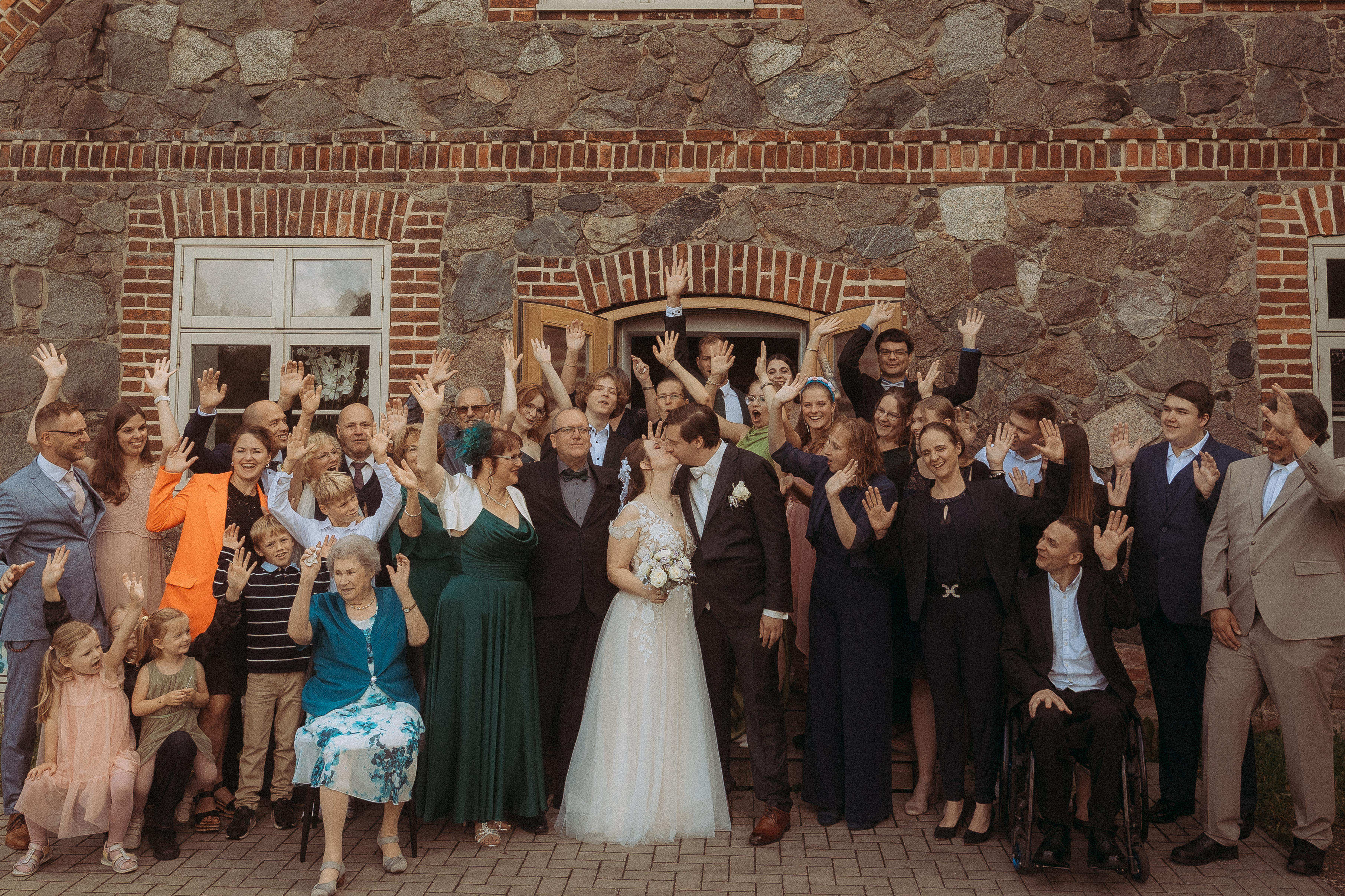 Hochzeitsgesellschaft feiert Brautpaar vor Backsteingebäude. Glückliche Menschen jubeln.