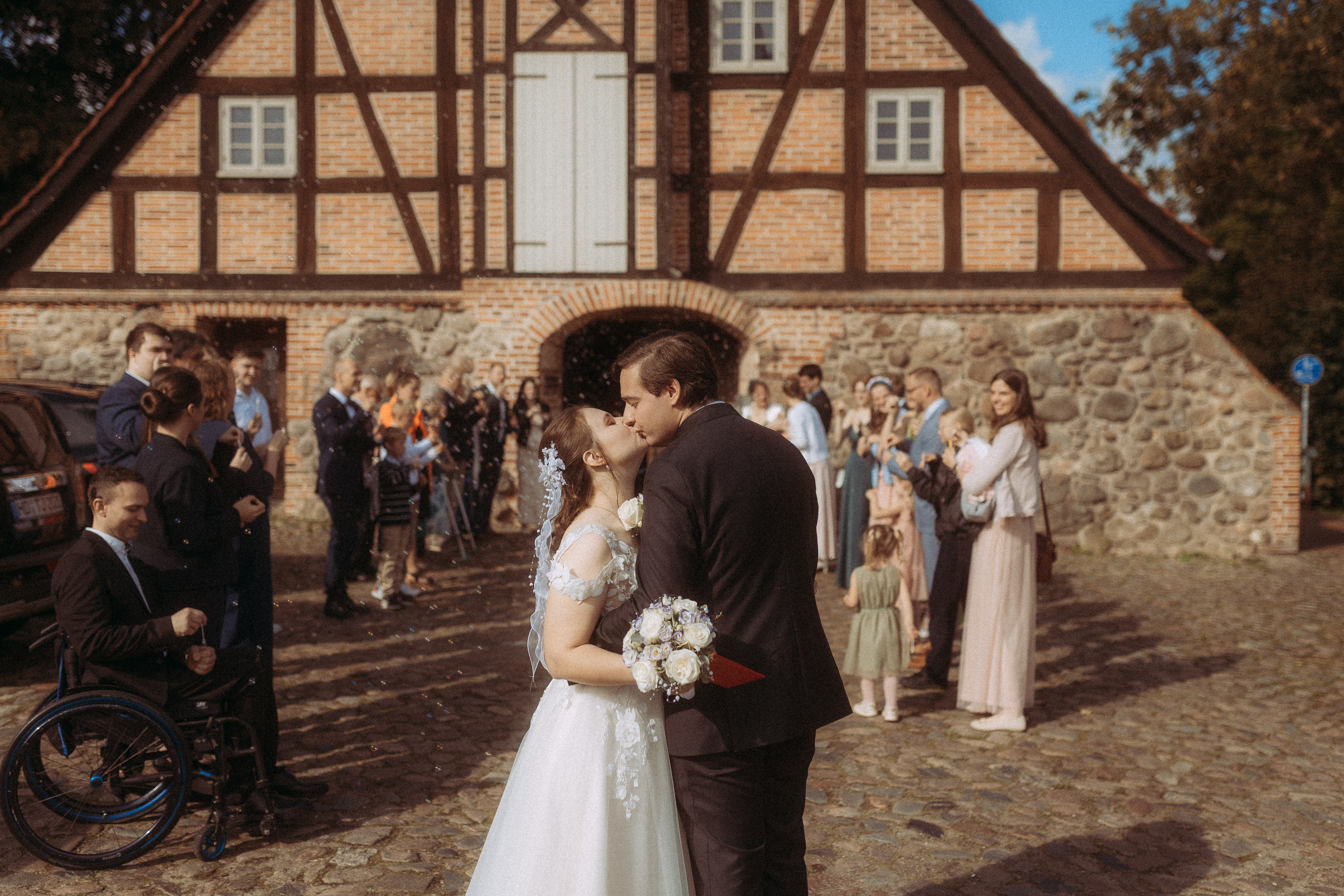 Brautpaar küsst sich vor dem Standesamt Friedland (MV), Gäste im Hintergrund. Hochzeit.