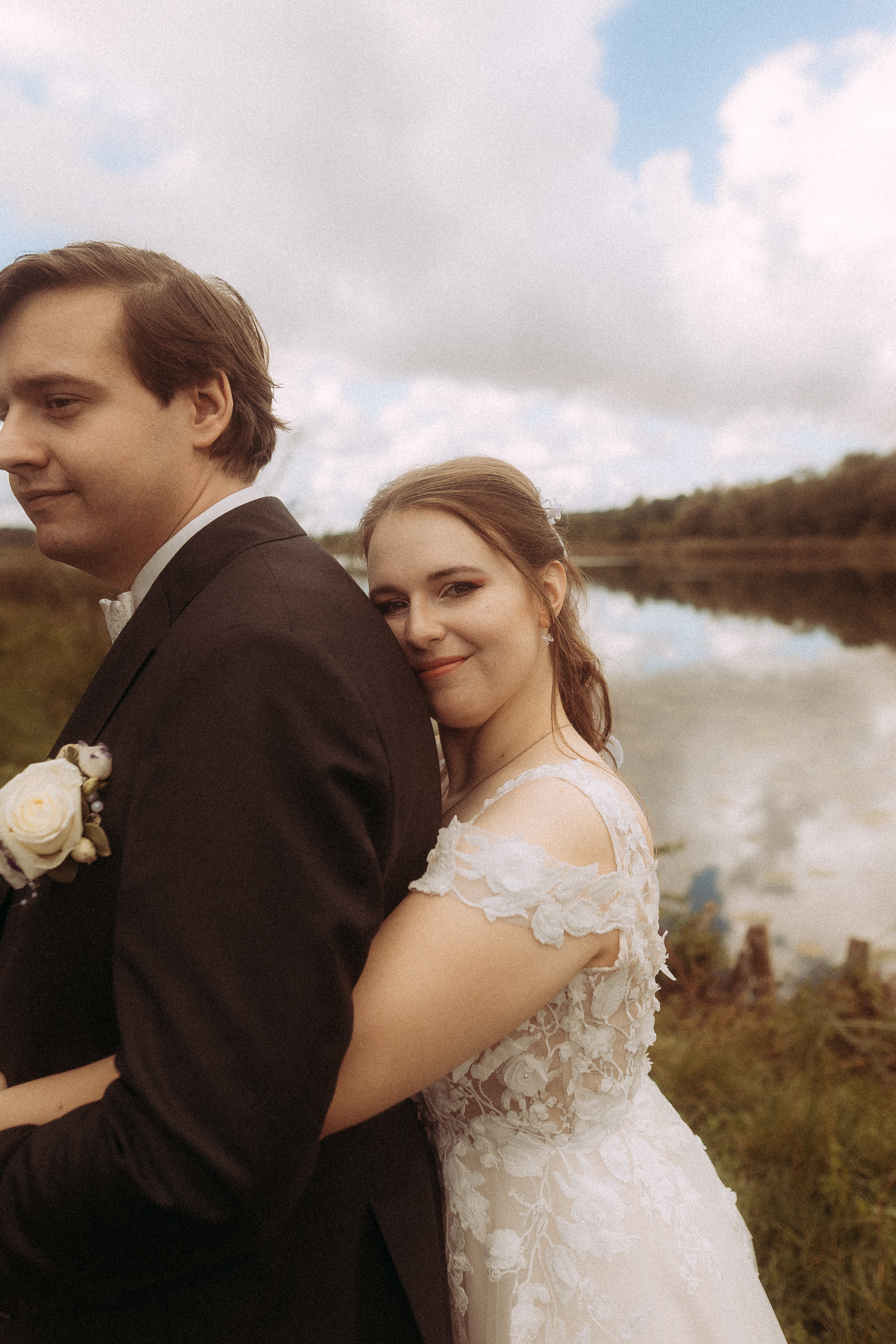 Brautpaar umarmt sich vor einem See. Die Braut lächelt in die Kamera.