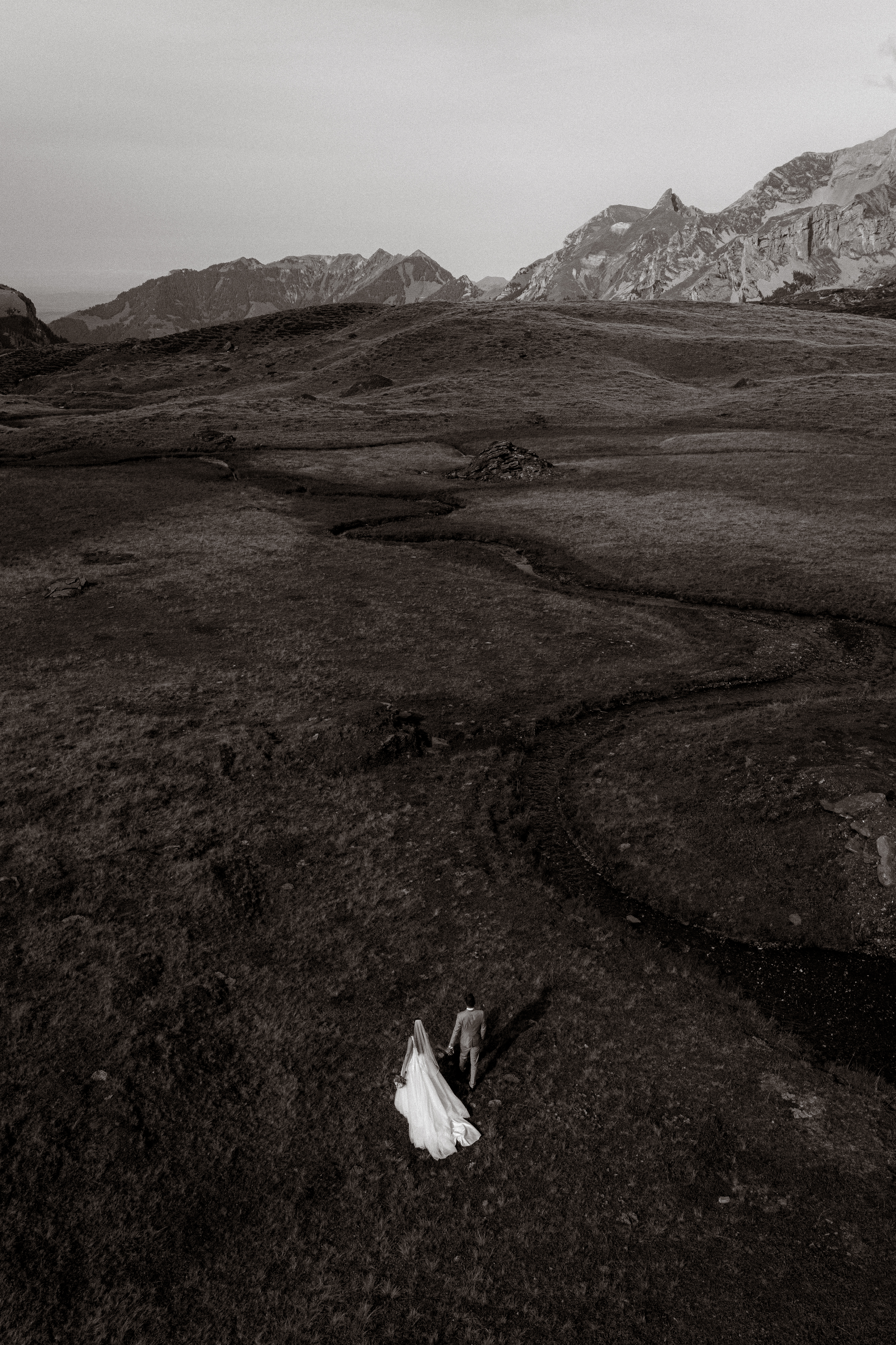 Hochzeitsfoto: Brautpaar wandert in dramatischer Berglandschaft.