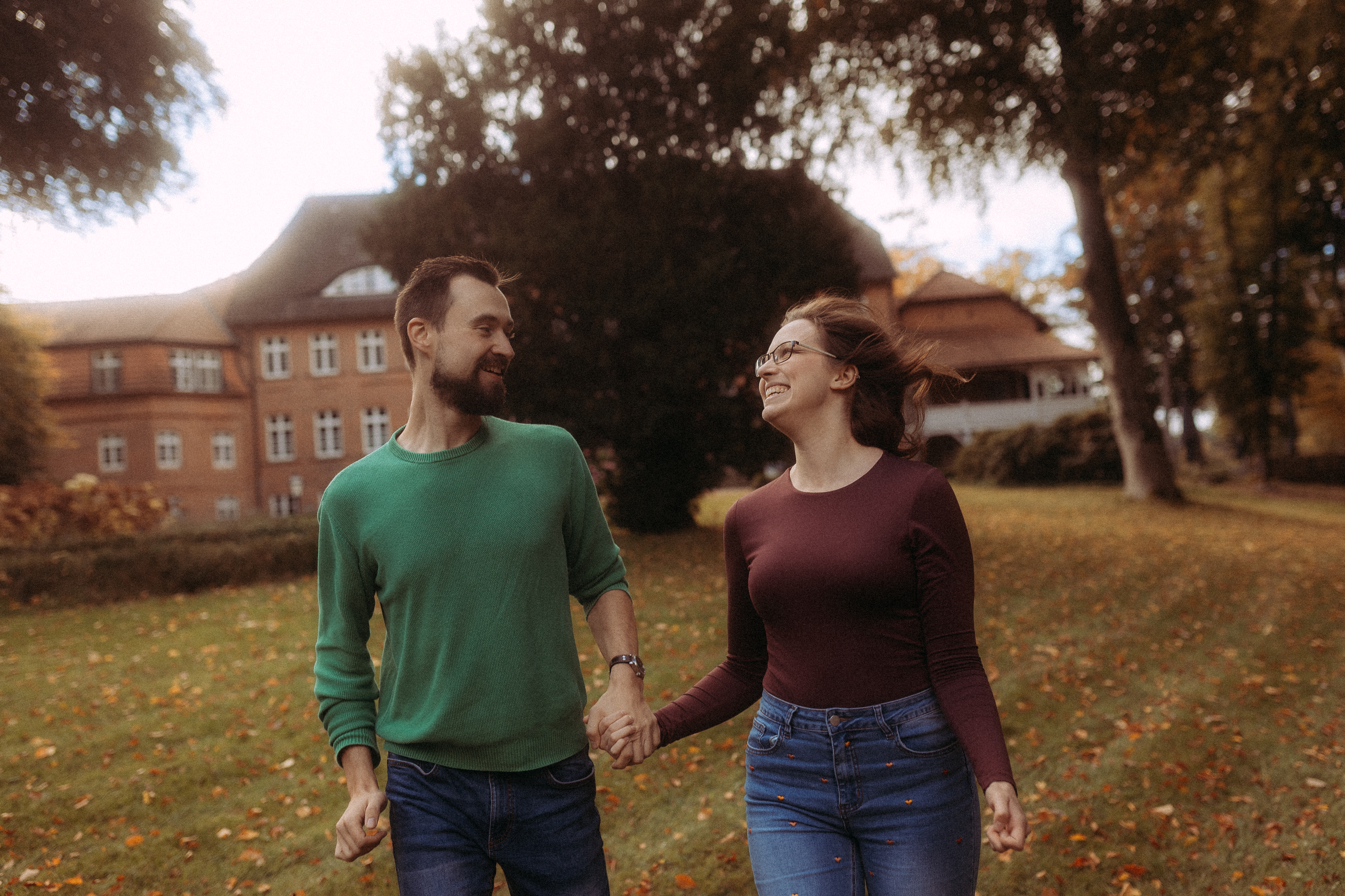 Glückliches Paar läuft Händchen haltend vor einem Haus im Herbst.