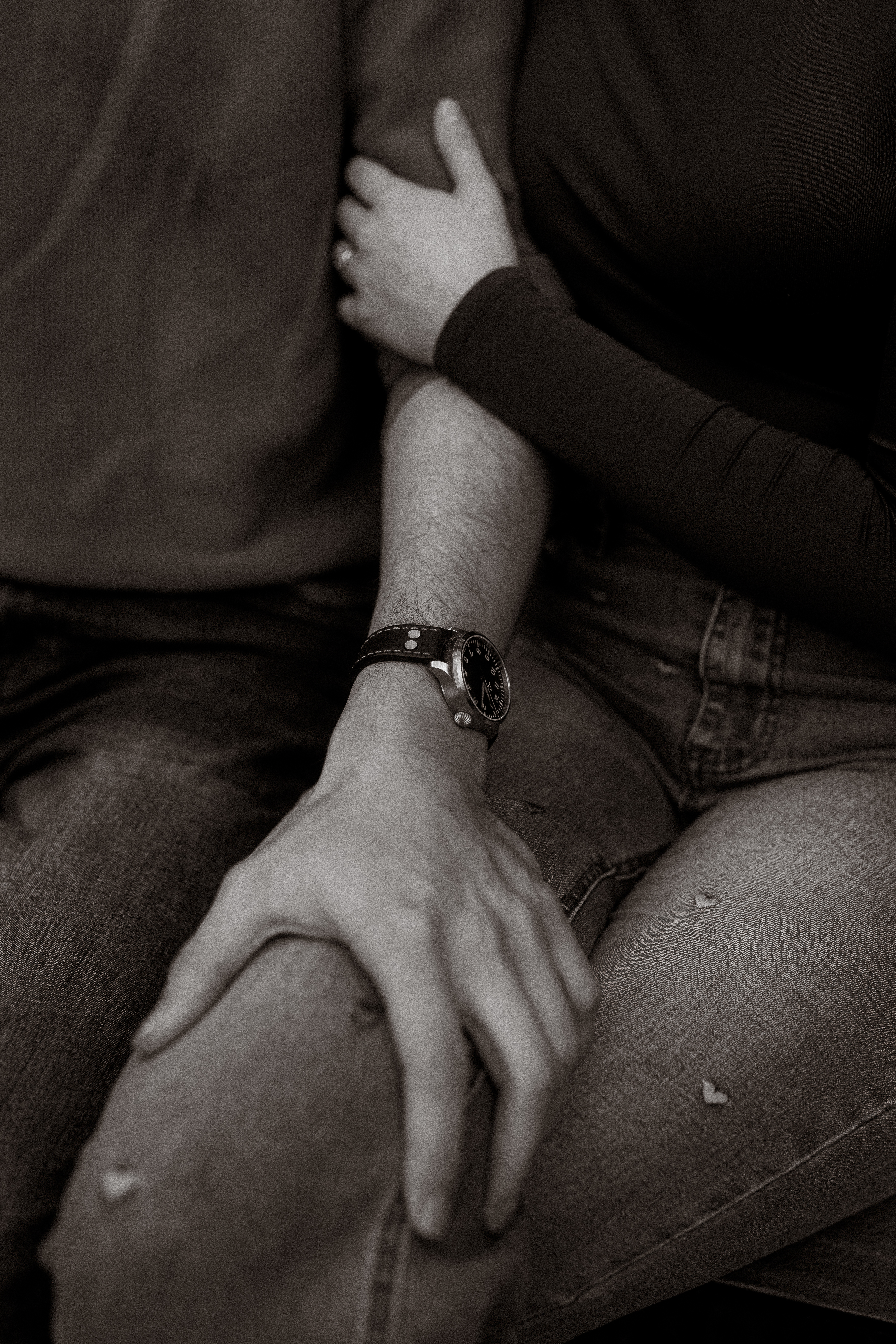 Pärchenshooting Basthorst: Paar sitzt eng umschlungen in Jeans, Armbanduhr sichtbar.