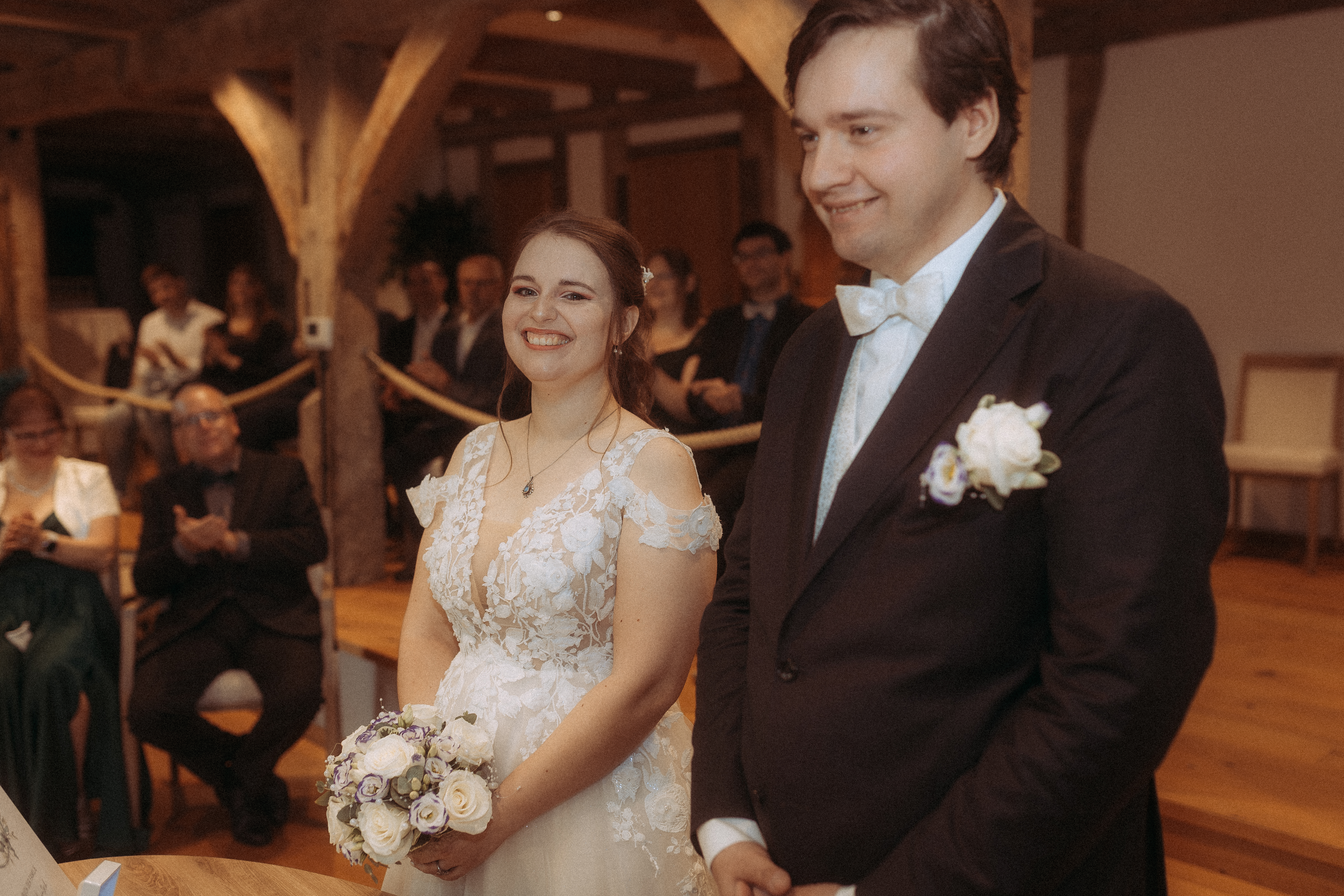Brautpaar bei standesamtlicher Hochzeit in Friedland (MV), glücklich lächelnd vor Gästen.