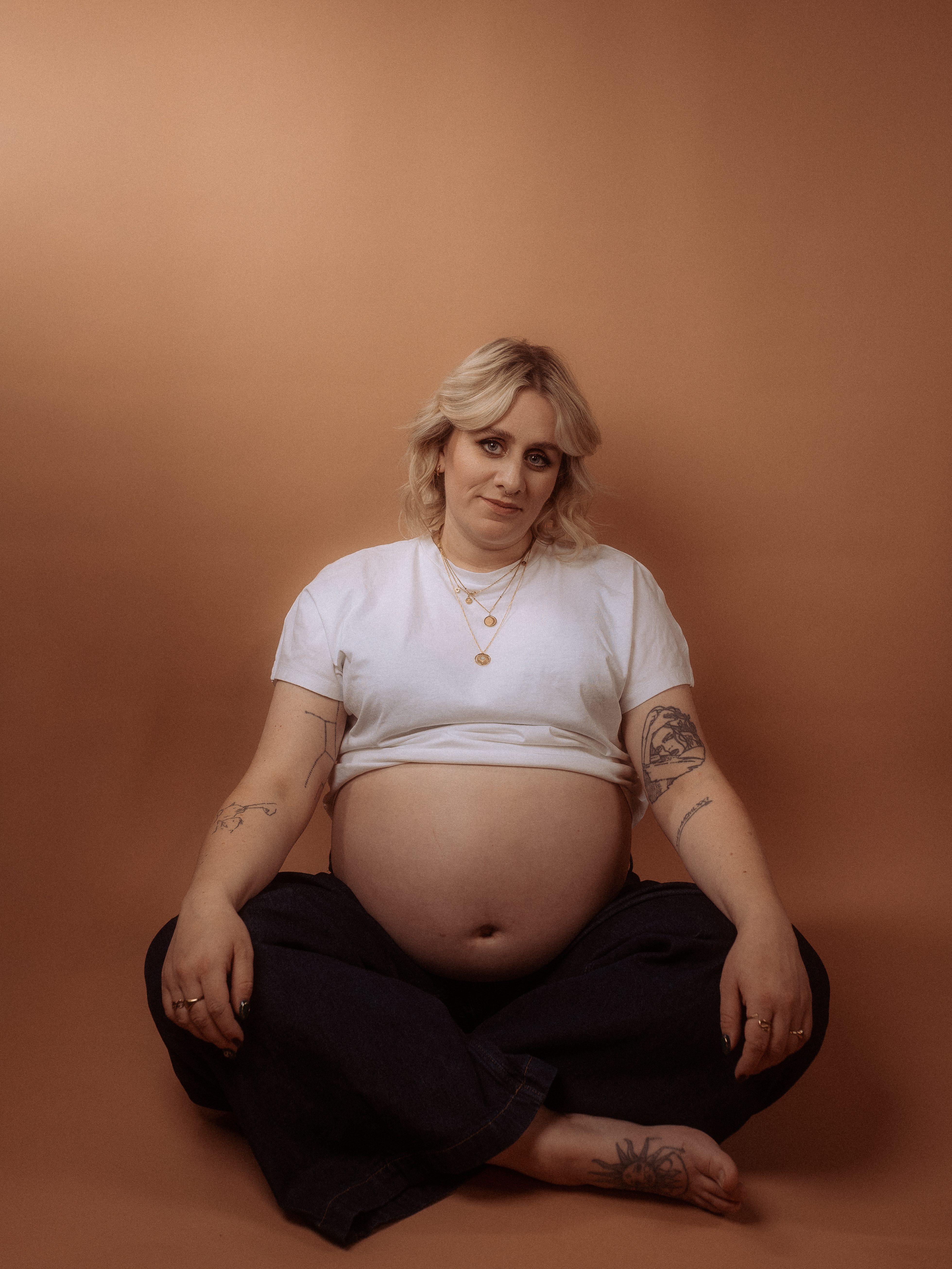 Schwangere Frau sitzt im Schneidersitz vor braunem Hintergrund. Babybauchshooting in Parchim.