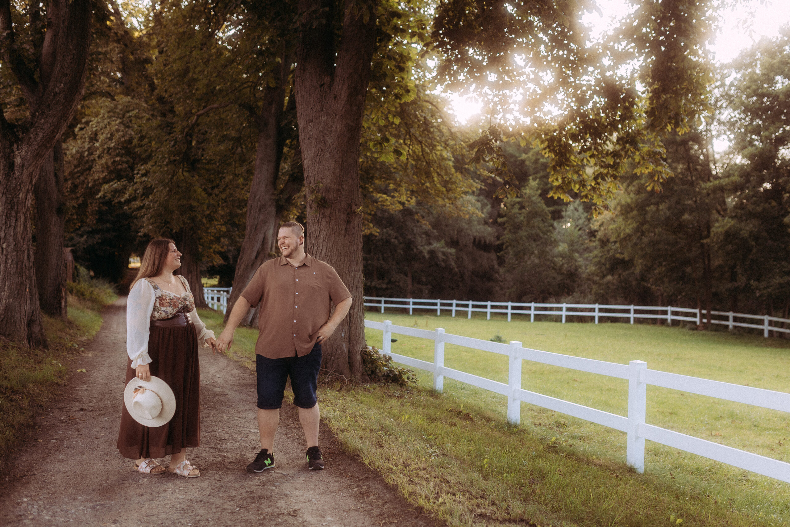 Pärchenfotos in Röbel: Paar Hand in Hand auf einem Weg mit Bäumen und weißem Zaun