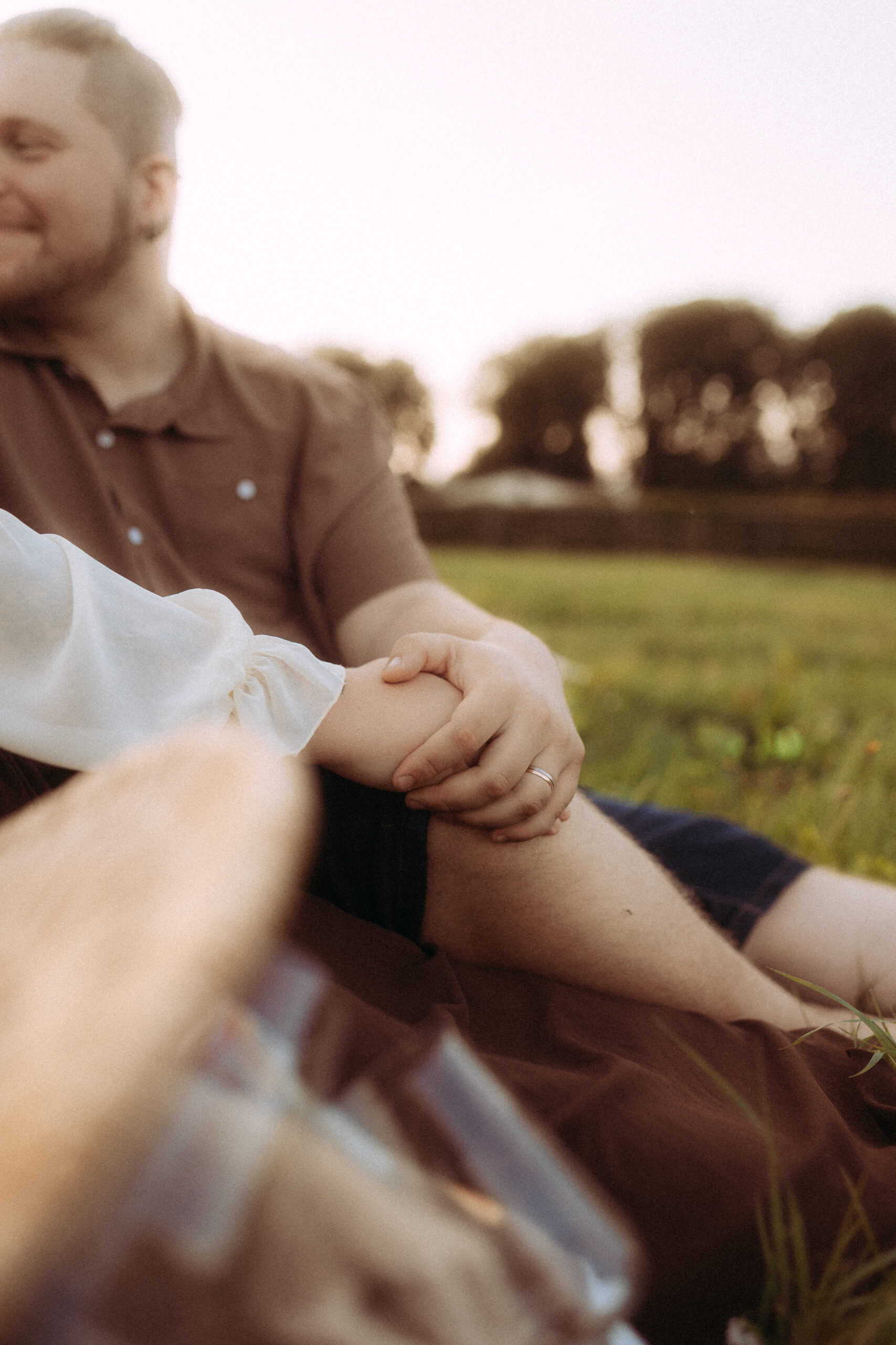 Pärchenfoto in Röbel: Paar sitzt im Gras, Hand auf Knie, Ehering sichtbar.