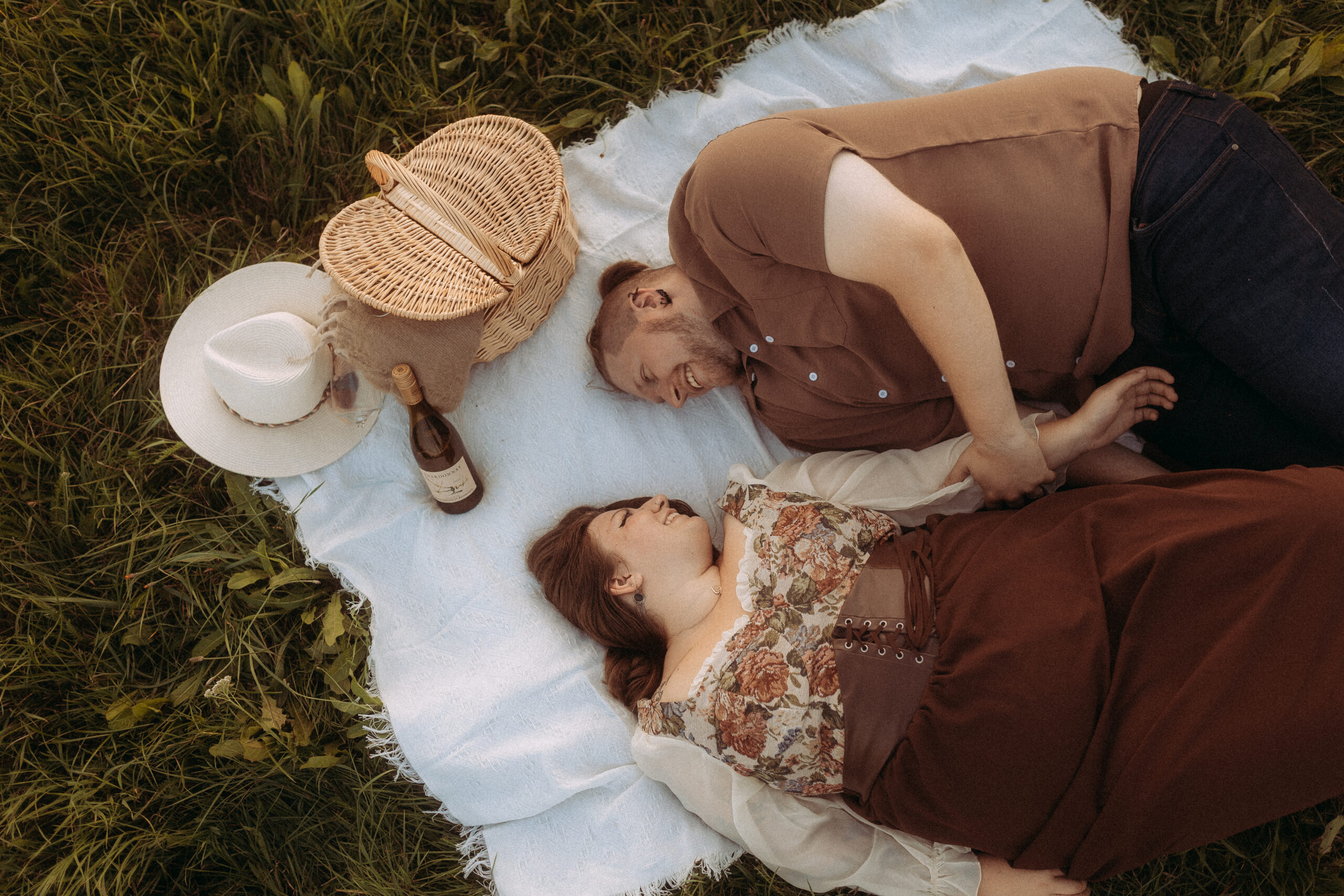 Lachendes Paar beim Picknick auf einer Decke im Grünen mit Korb und Hut