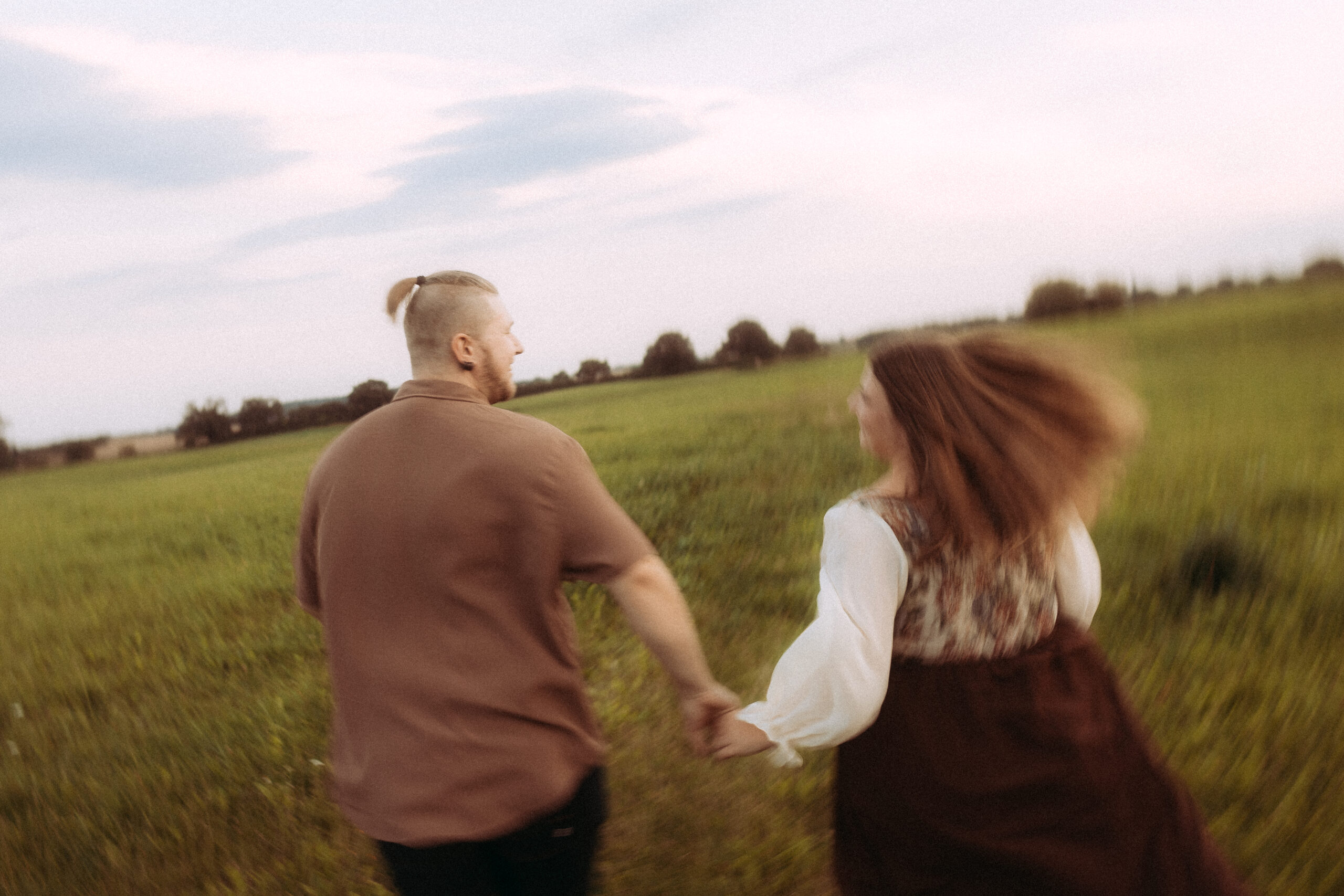 Lächelndes Paar läuft Hand in Hand über eine grüne Wiese.