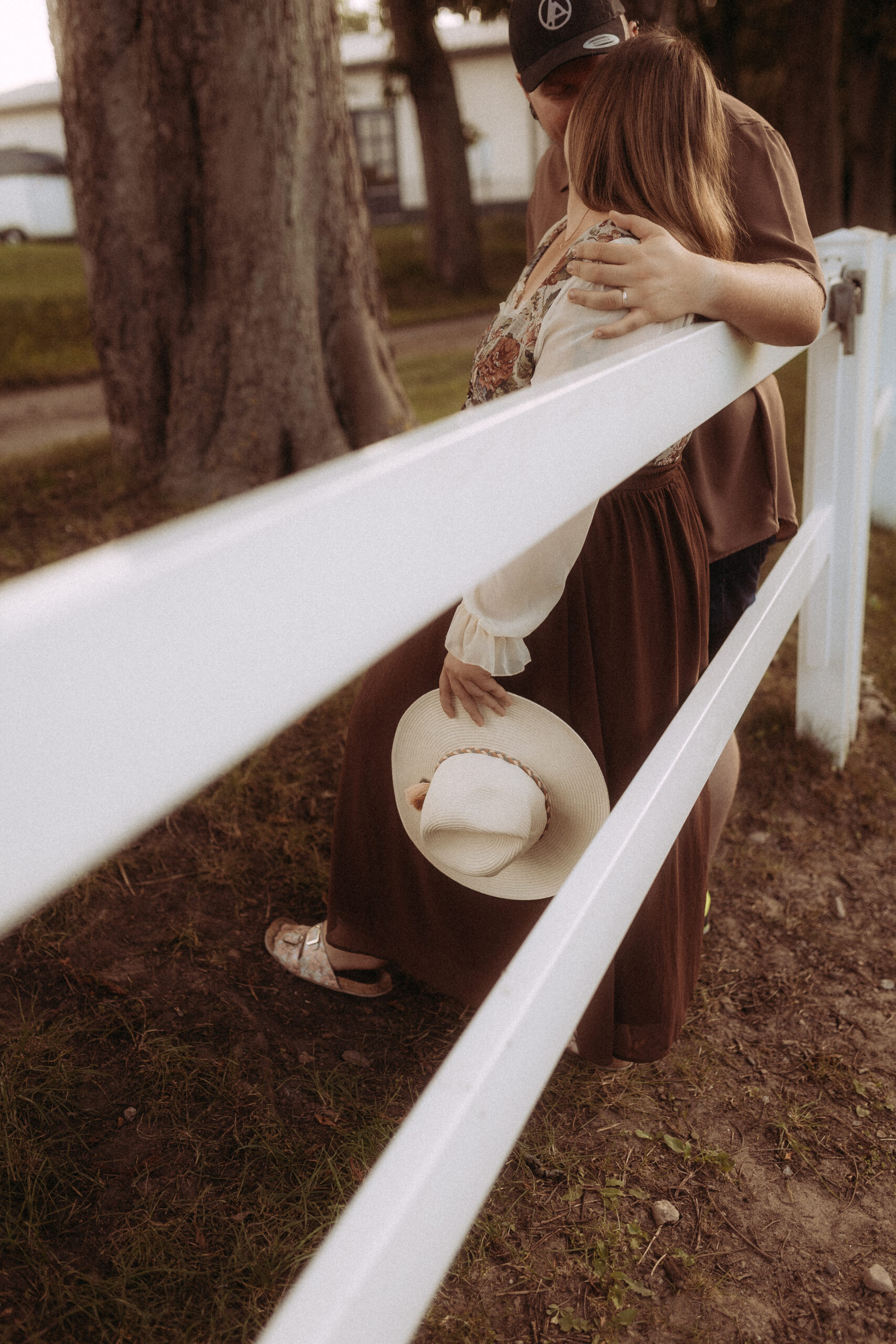Pärchenfoto in Röbel: Paar umarmt sich an weißem Zaun, Frau hält Hut.