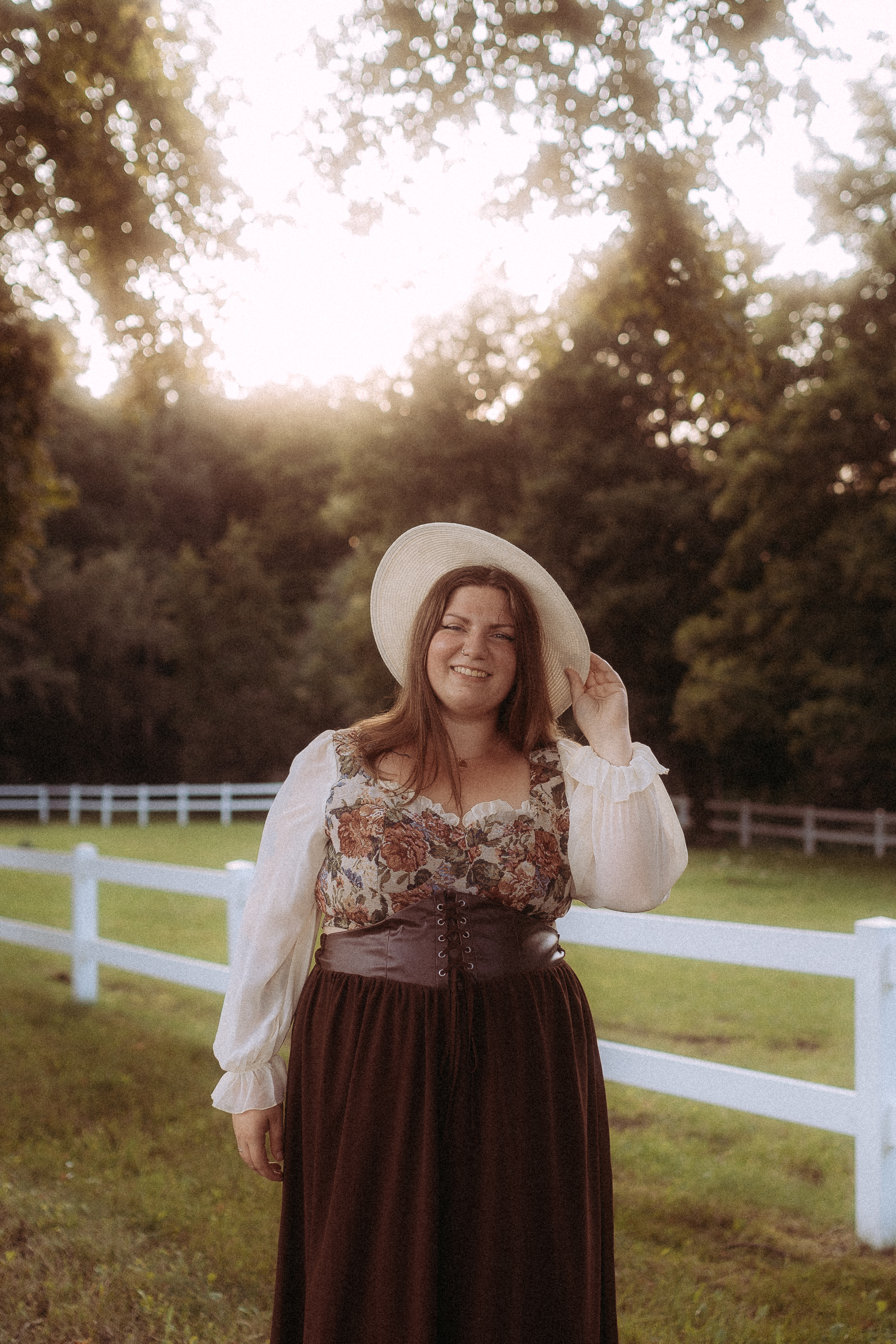 Frau mit Hut, Bluse und braunem Rock vor weißem Zaun. Pärchenfotos in Röbel.