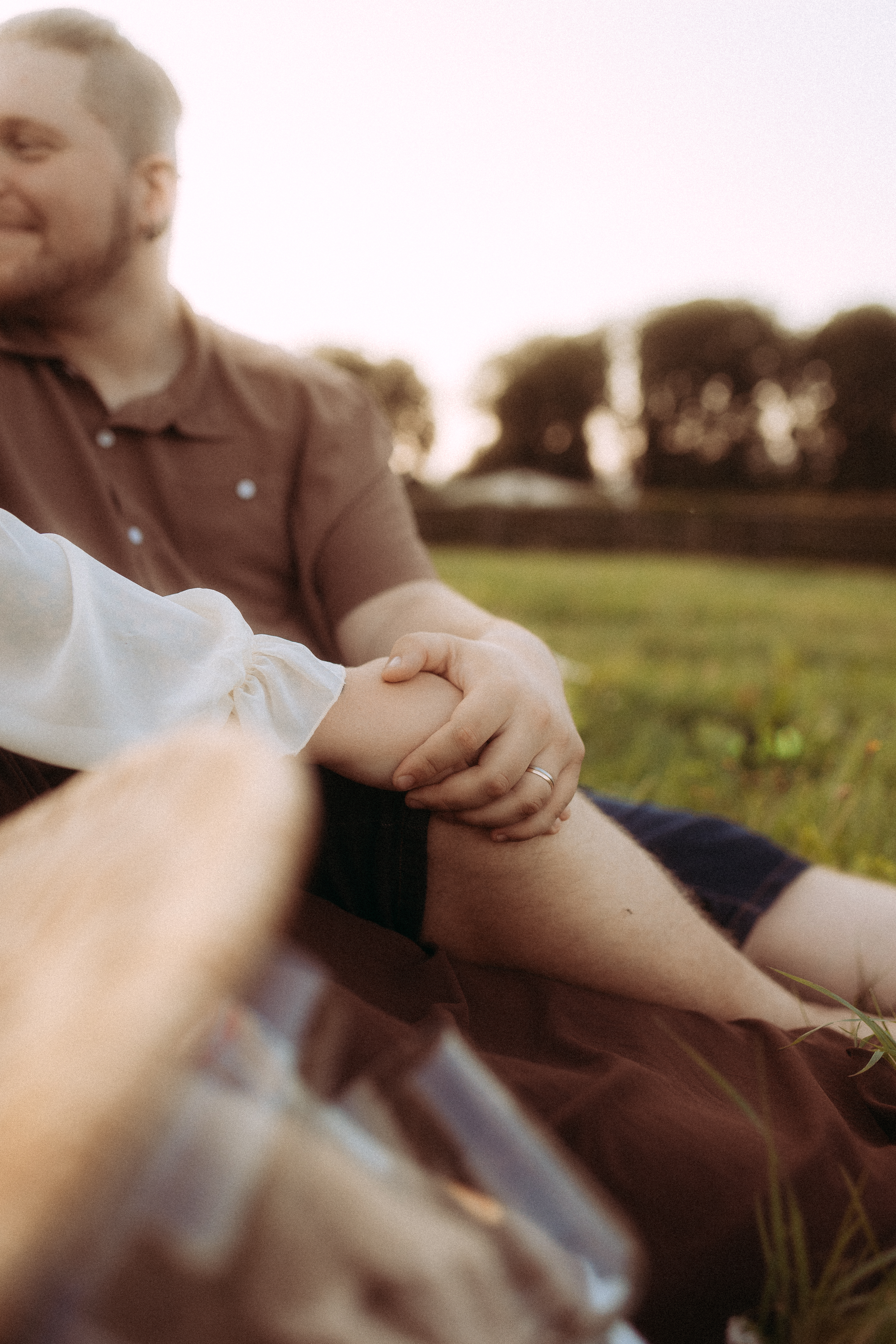 Pärchenfoto in Röbel: Paar sitzt im Gras, Hand auf Knie, Ehering sichtbar.