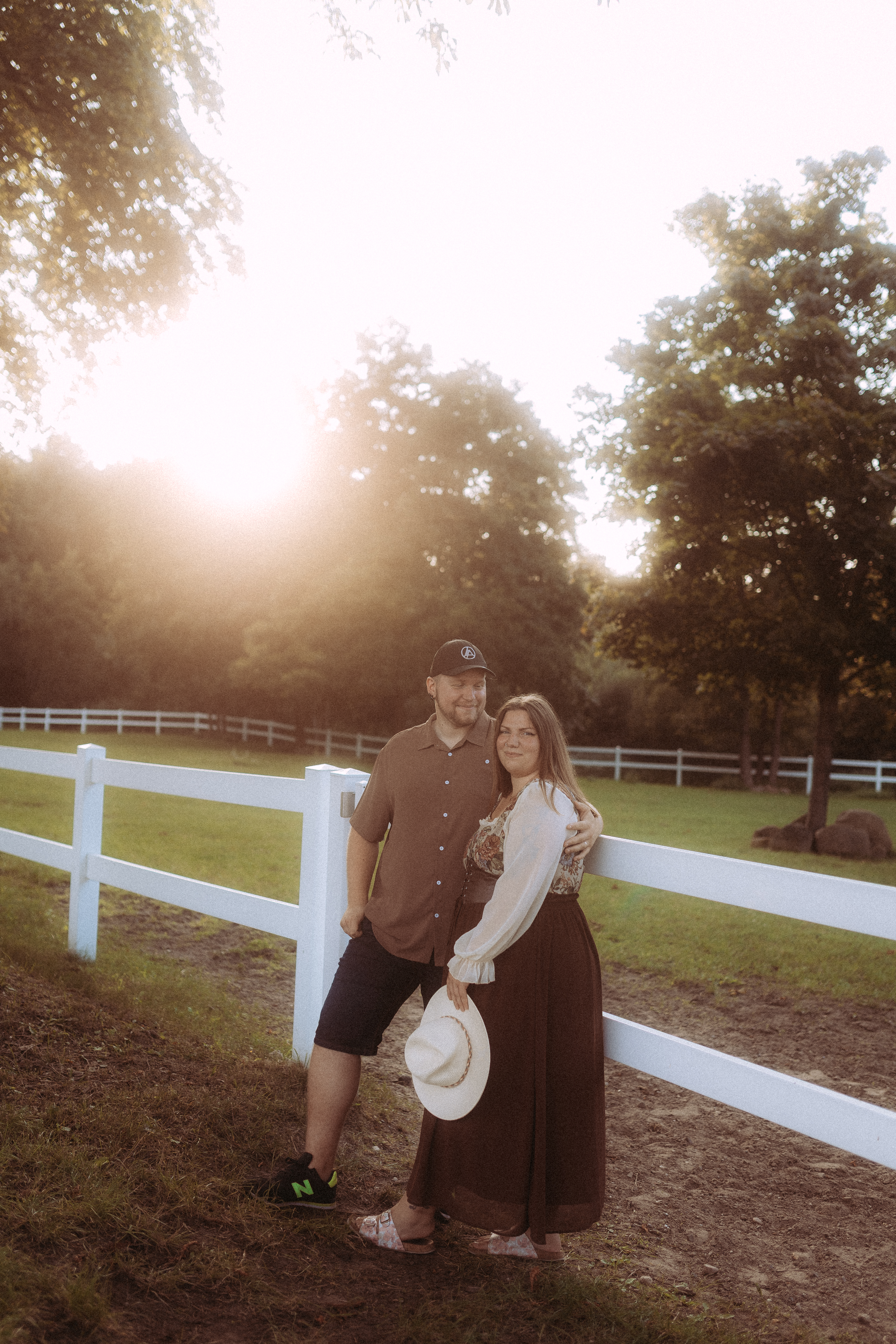 Pärchenfotos in Röbel: Paar am weißen Zaun im Grünen, warmer Sonnenschein.