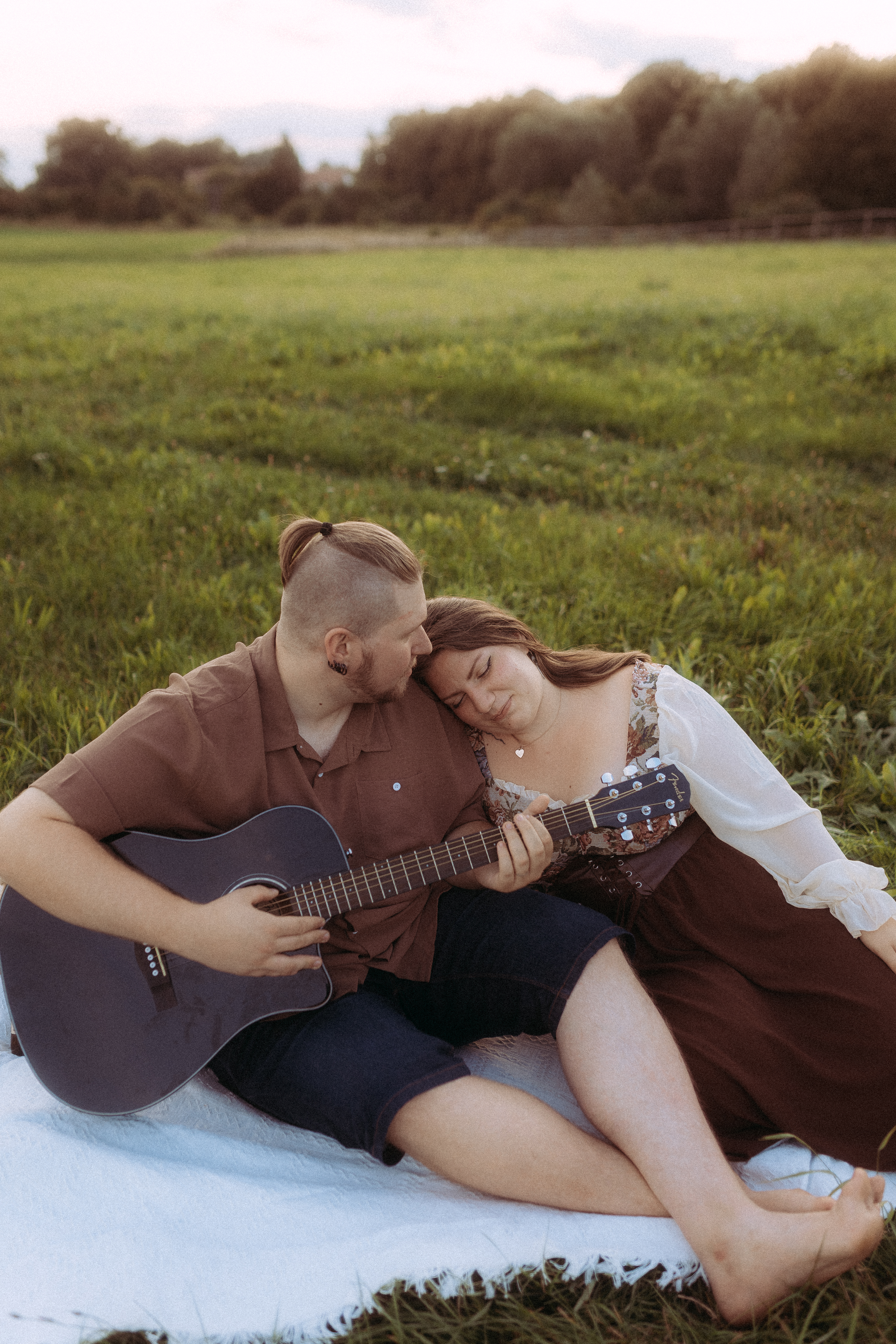 Pärchen sitzt in Röbel auf einer Wiese, Mann spielt Gitarre, Frau lehnt an ihm.