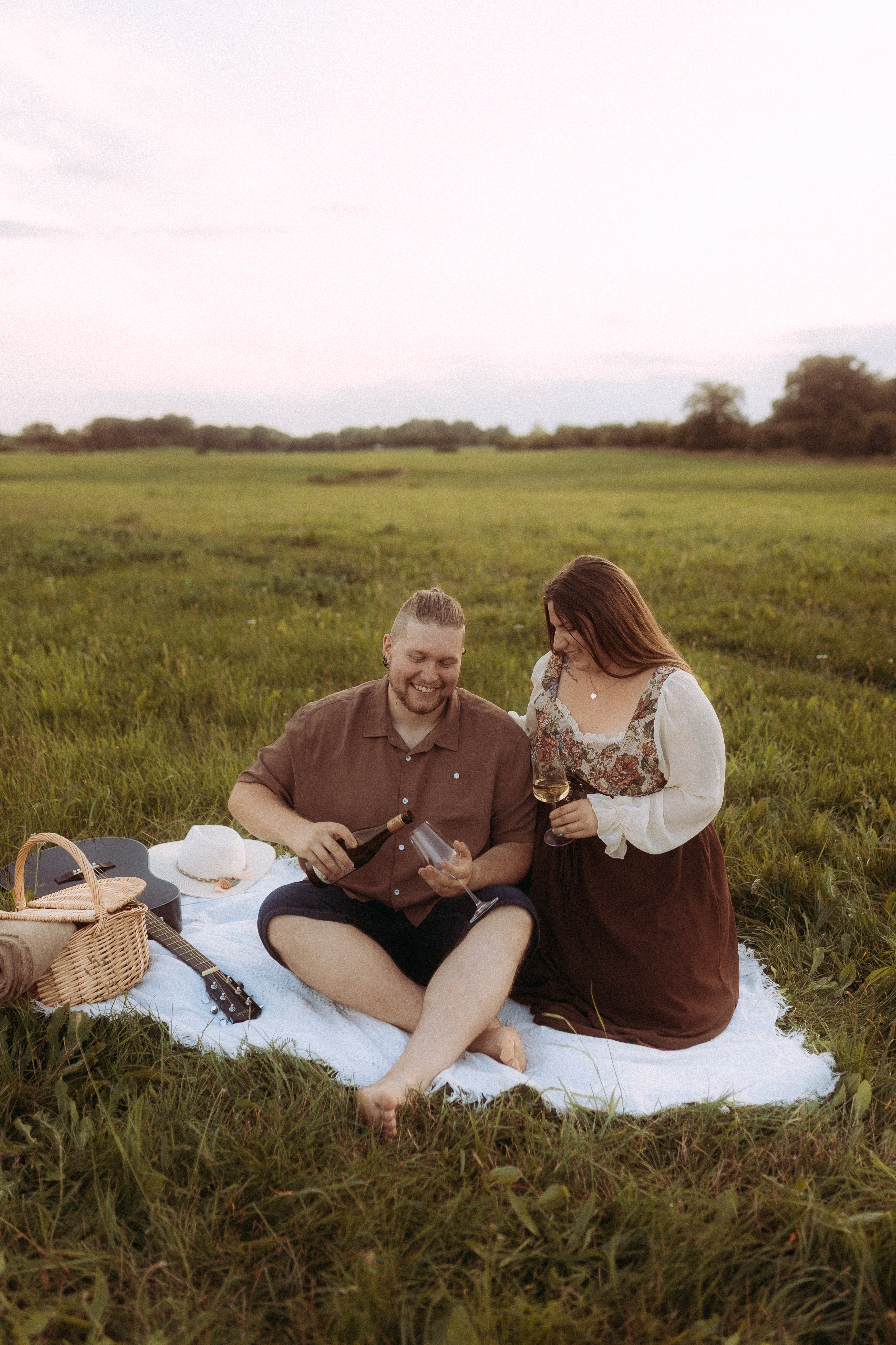 Pärchen genießt Wein bei einem Picknick in Röbel. Gitarre und Korb im Gras.