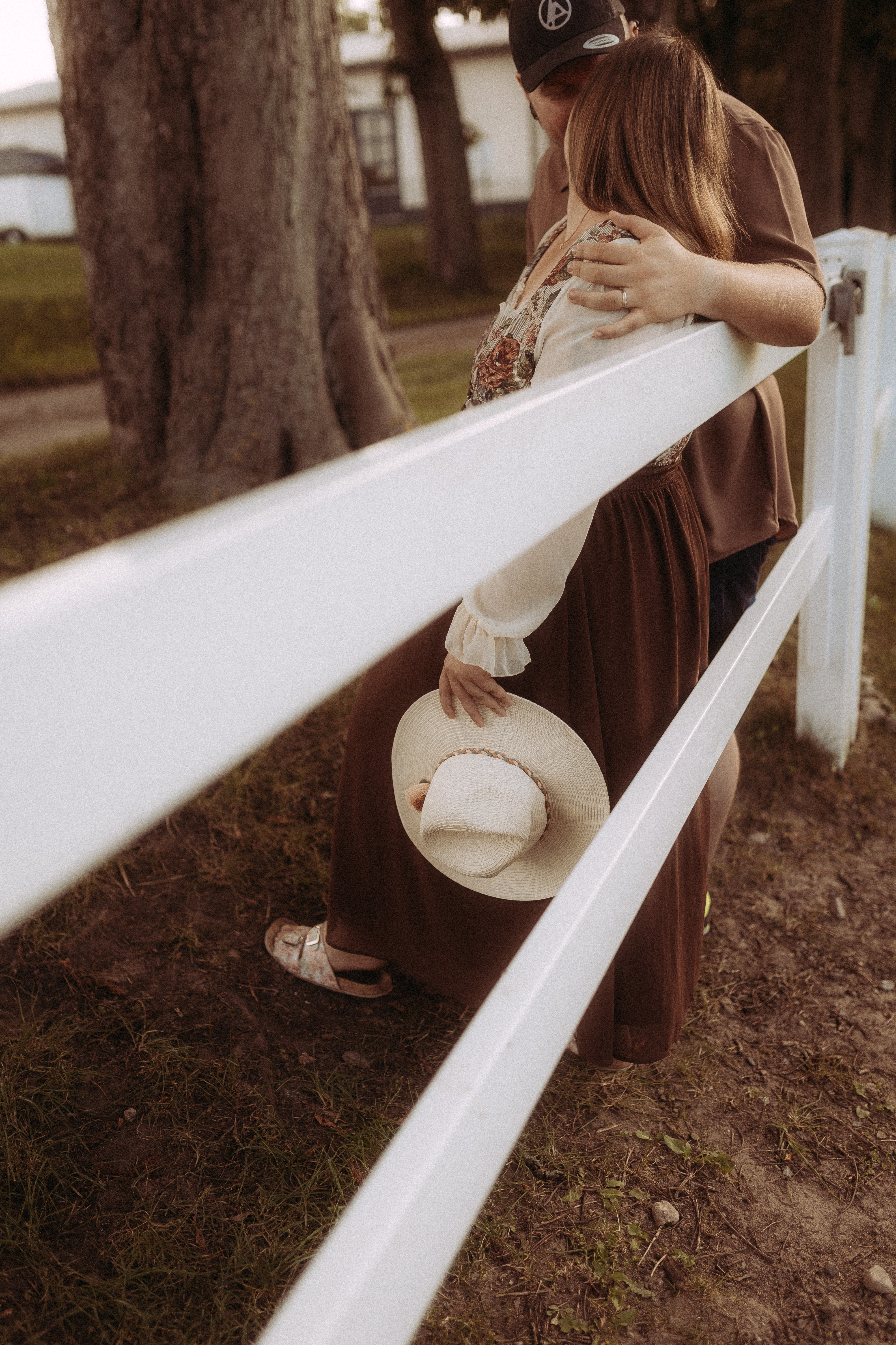 Pärchenfoto in Röbel: Paar umarmt sich an weißem Zaun, Frau hält Hut.