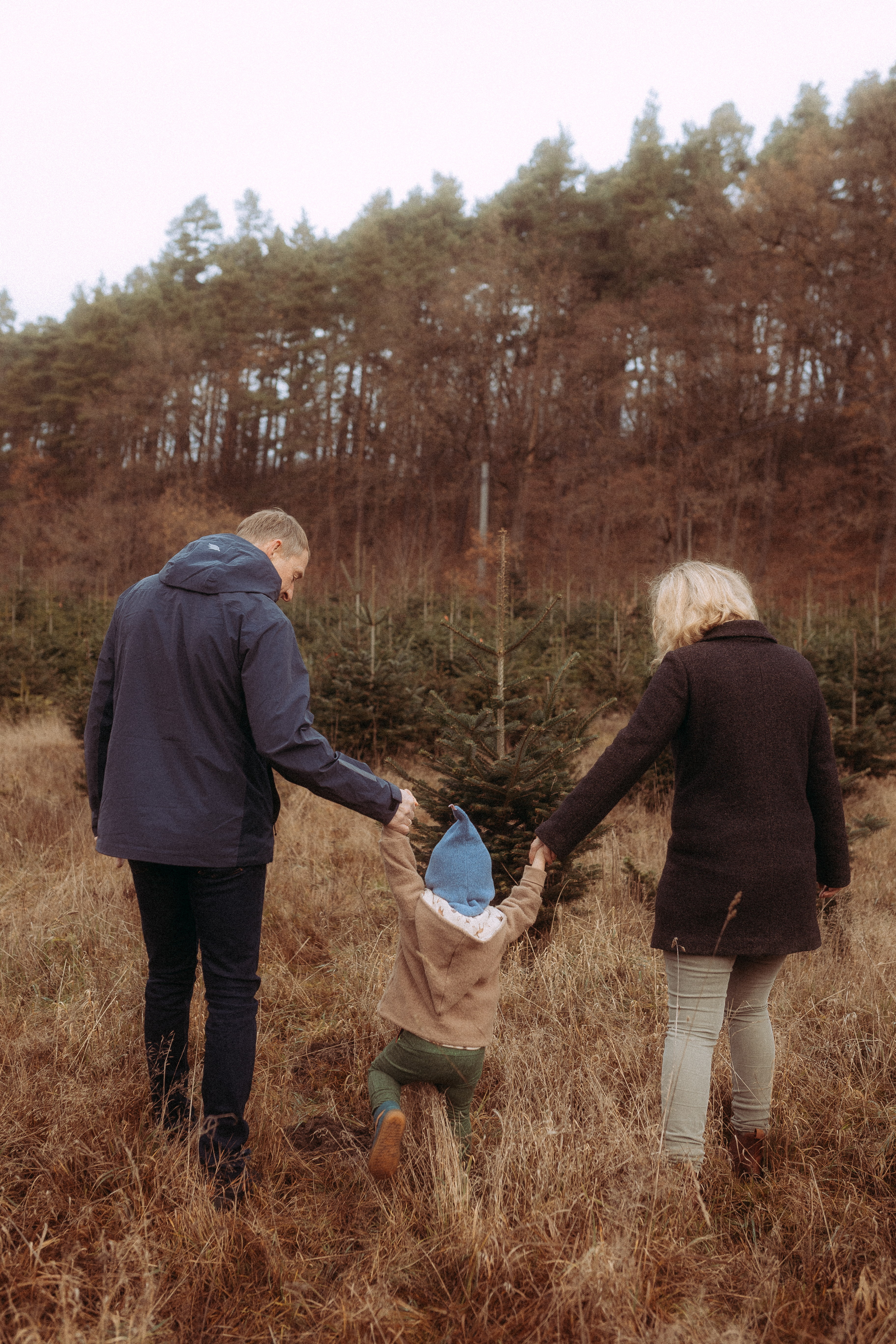 Familie spaziert in Basthorst auf Wiese mit Bäumen im Hintergrund. Pärchenshooting.